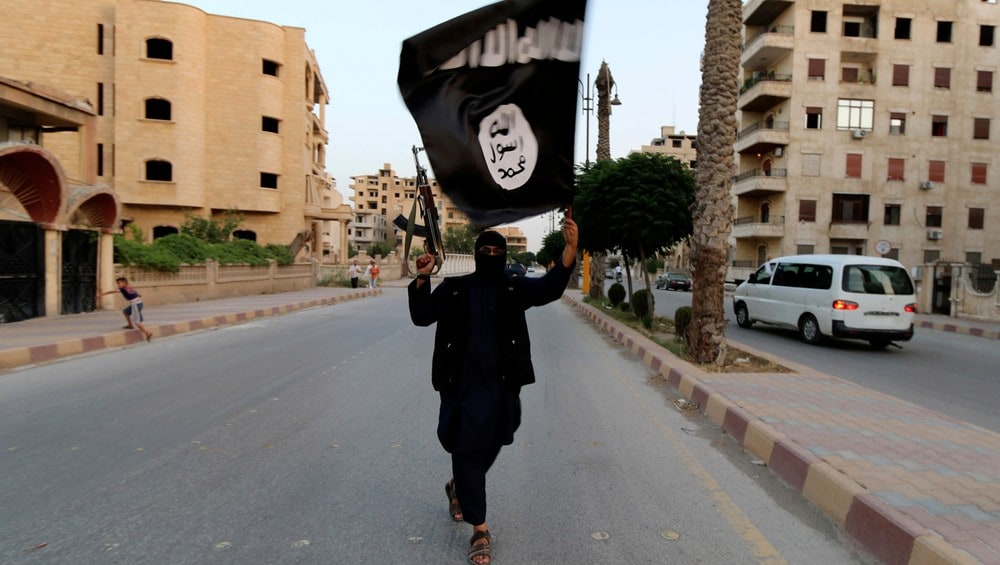 Et medlem av ISIL løfter opp et ISIL-flagg i den syriske byen Raqqa