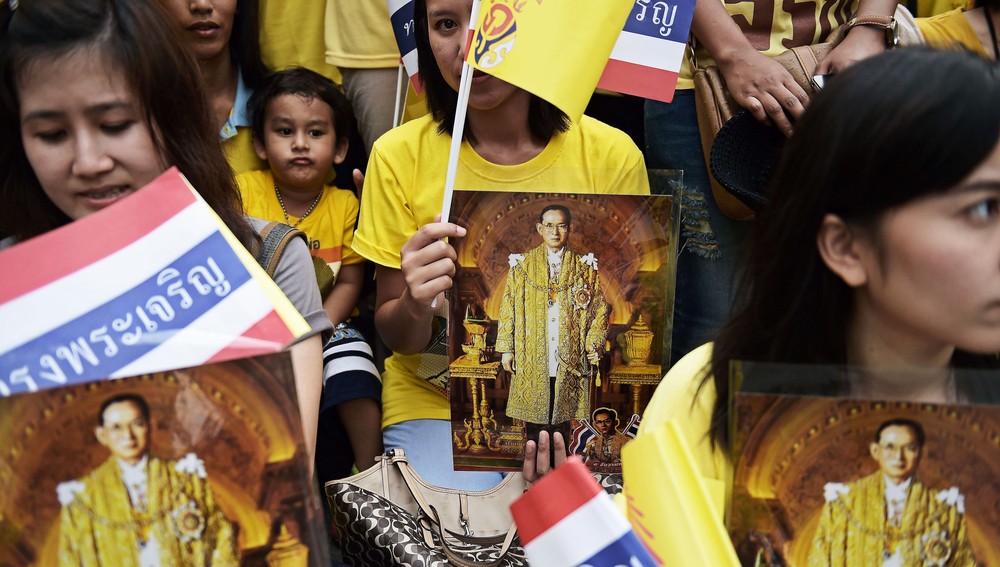 Demonstranter med kongebilder - Thailandsk politikk er delt opp i «gulskjorter» og «rødskjorter». Gulskjortene er kongetro og støtter militærjuntaen. På bildet vinker noen gulskjorter med flagg mens de holder bilder av kong Bhumibol på 87-årsdagens hans, 5. desember i fjor. - Foto: Christophe ARCHAMBAULT / AFP