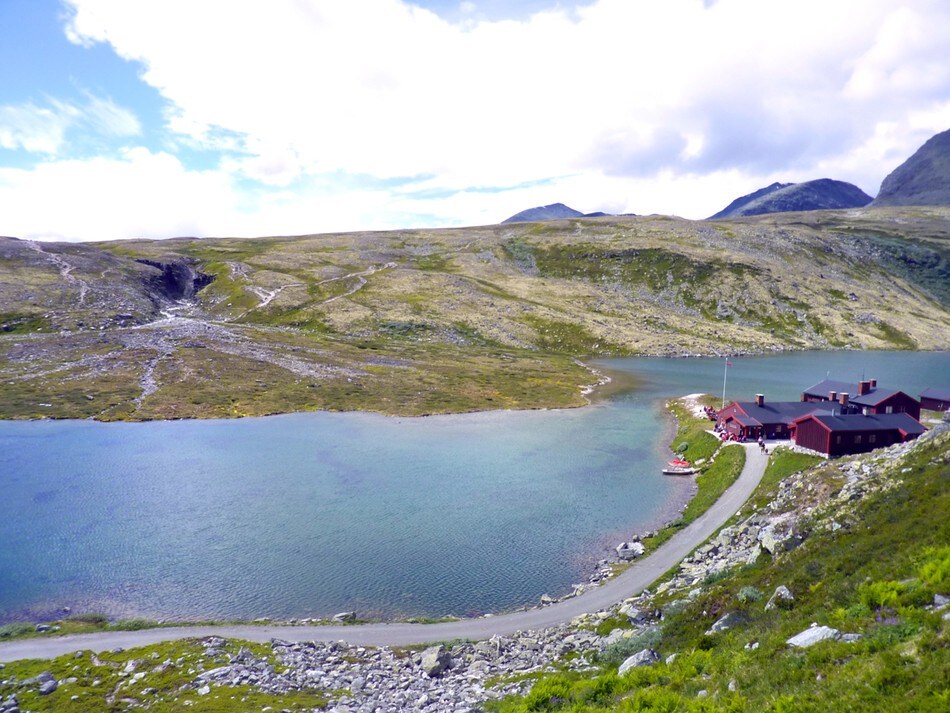 Rondvassbu i Rondane. Hytta synes godt til høyre og Jutulhogget til venstre. Besøkende sitter ute i solveggen og nyter dagen.