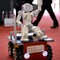 En liten robot i en robotbil vinker til publikum på åpningsdagen. 