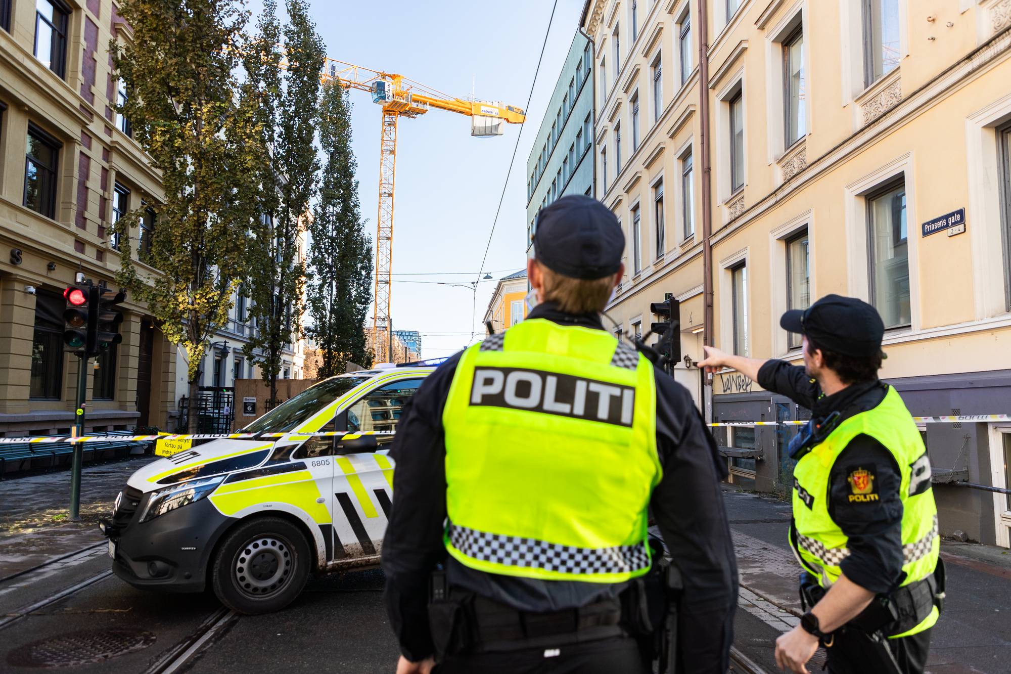 Politibetjenter står ved en politibil sperret av med bånd i Prinsens gate, mens en kran er synlig. (Bildebeskrivelsen er laget av en KI-tjeneste)