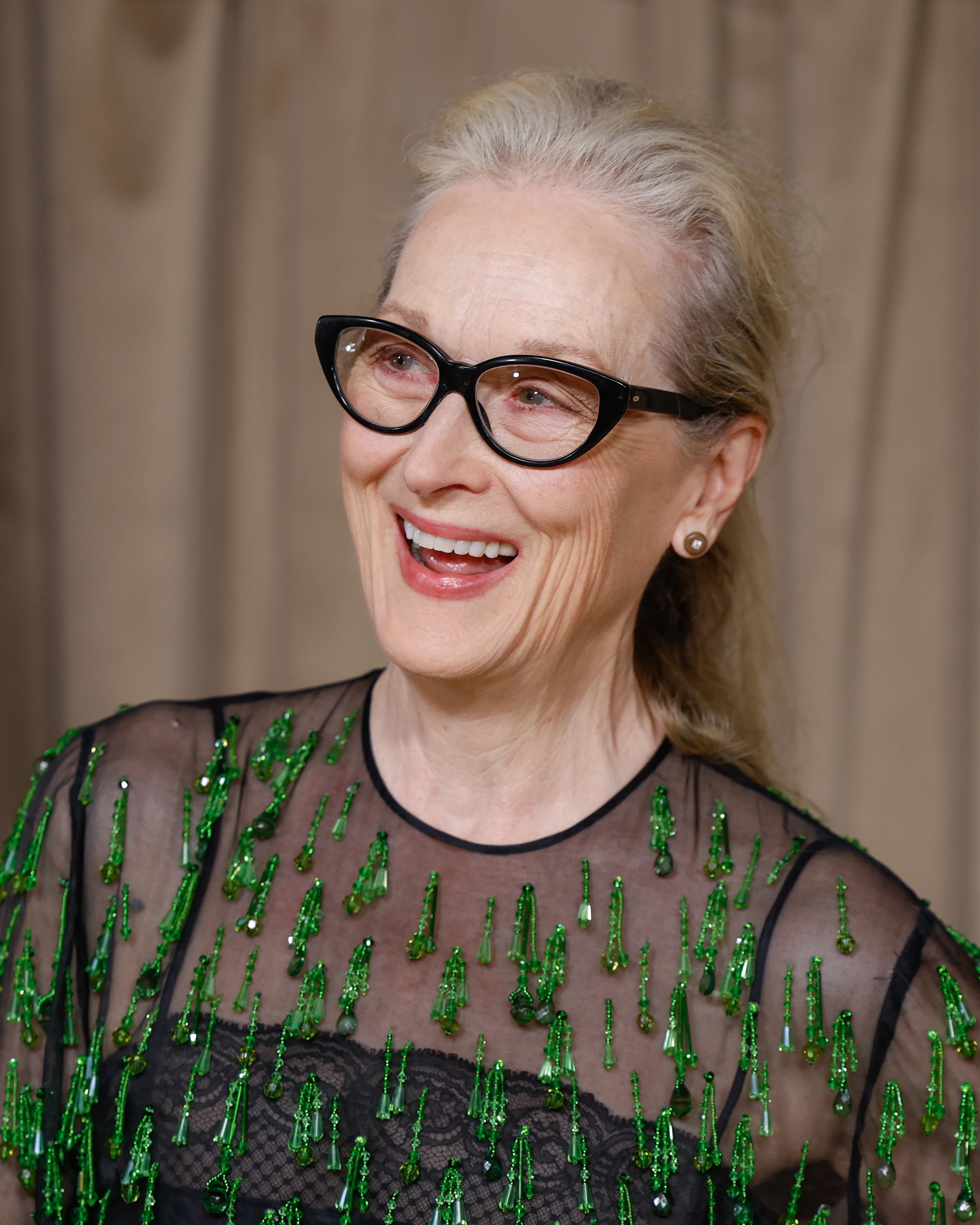 Skuespiller Meryl Streep smiler iført briller og en svart kjole med grønne detaljer. (Bildebeskrivelsen er laget av en KI-tjeneste)