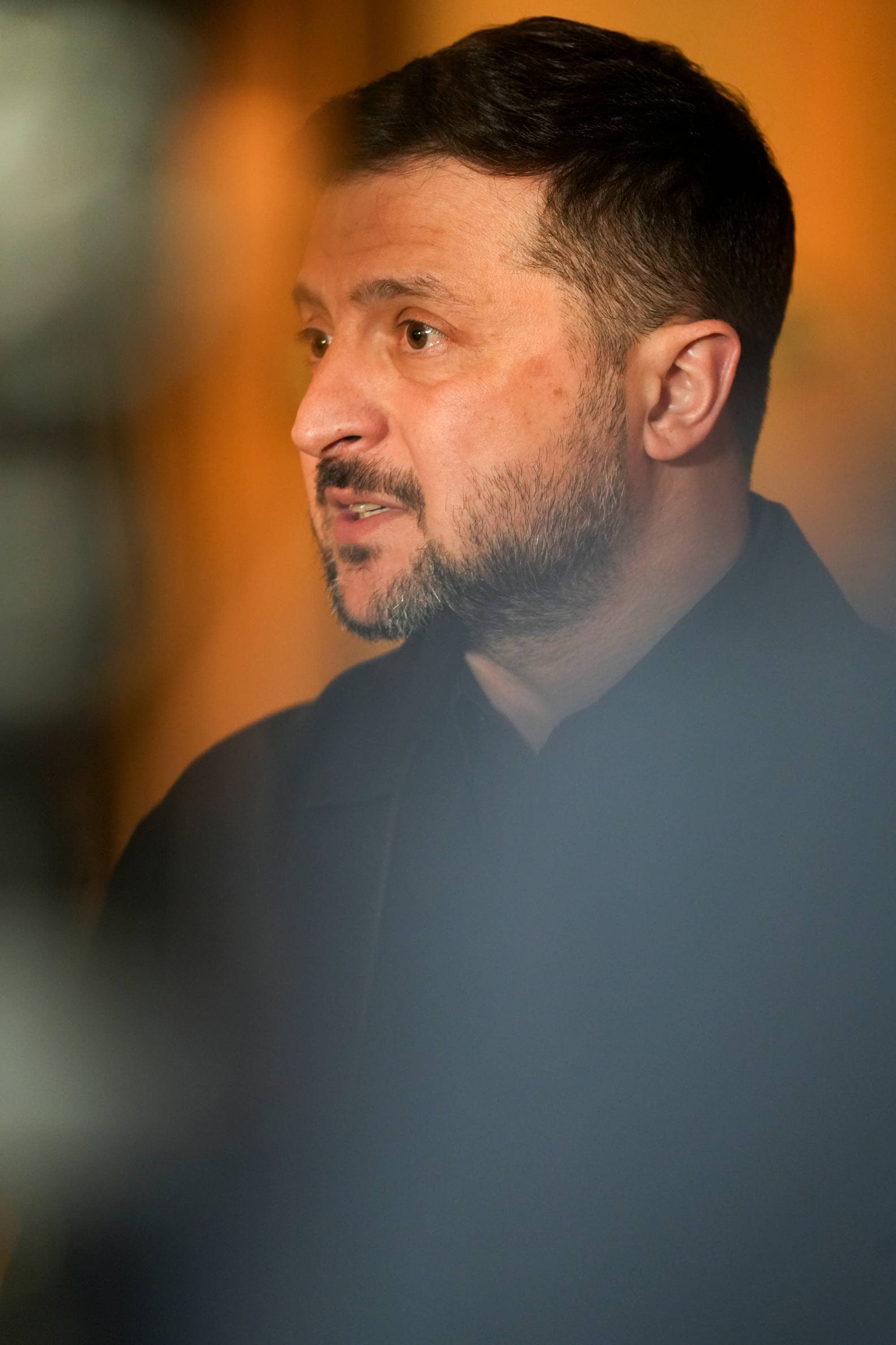 Ukrainas president Volodymyr Zelenskyj. Han er i profil og ser til venstre. Bakgrunnen er uskarp og oransje. (Bildebeskrivelsen er laget av en KI-tjeneste)
