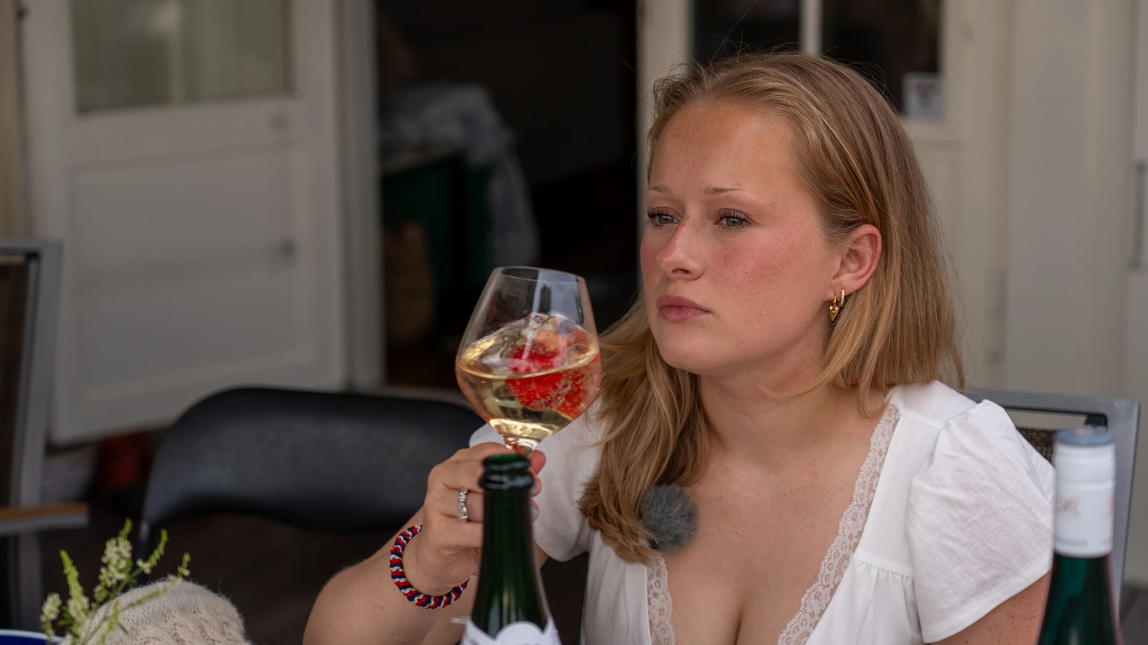 En kvinne sitter ved et bord og holder et glass med drikke. (Bildebeskrivelsen er laget av en KI-tjeneste)
