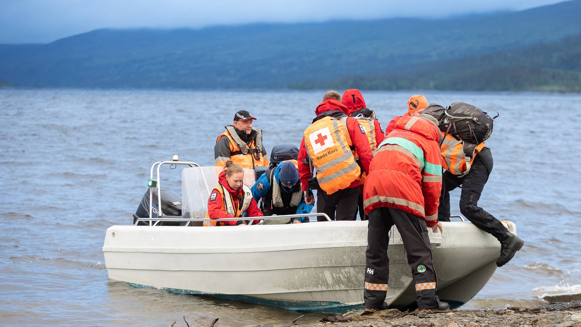 Letepersonell i en båt på Funnsjøen. Flere sitter allerede i båten, mens en person i front hjelper de siste om bord.