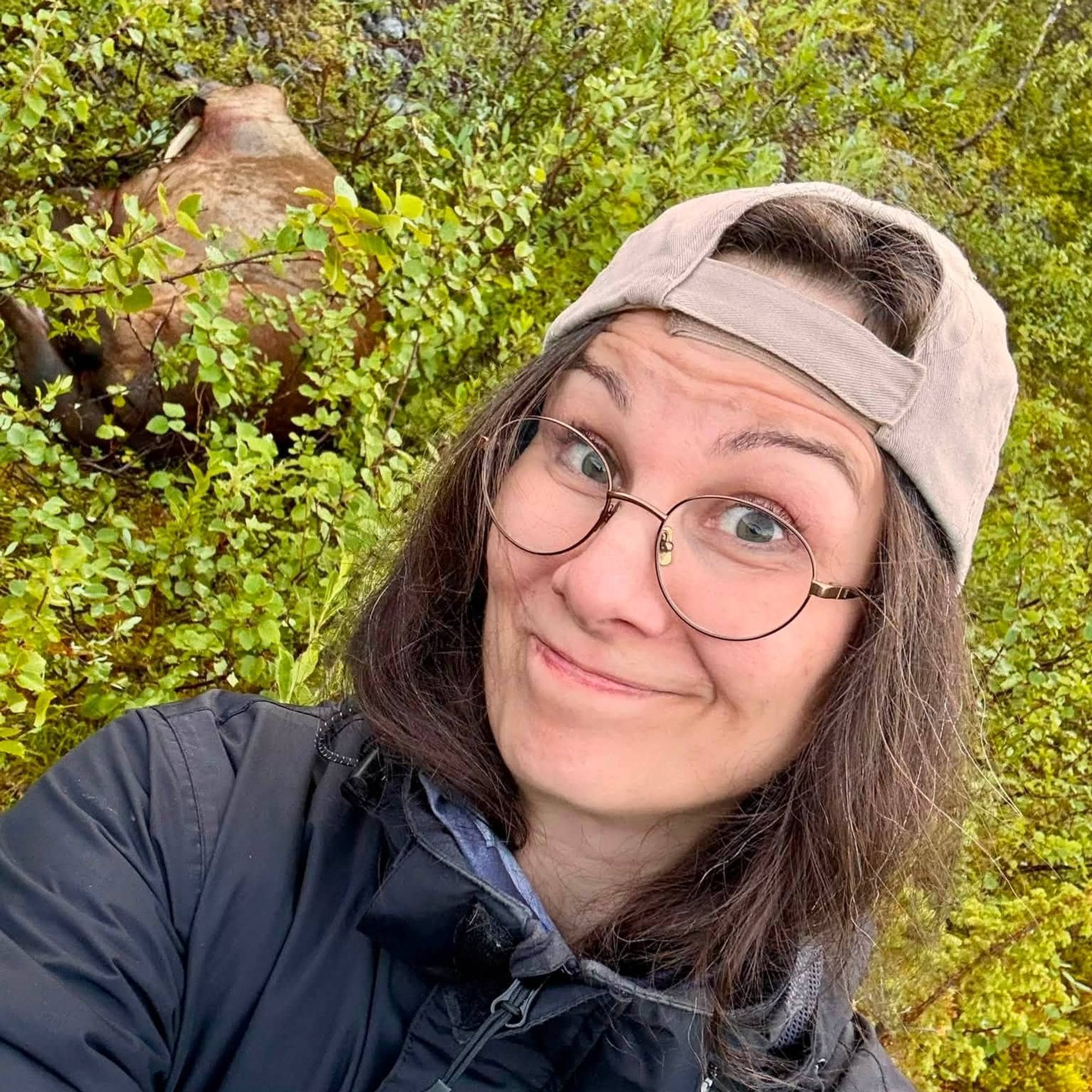En dame med capsen bak frem tar en selfie med en hvalross som ligger i skogen.