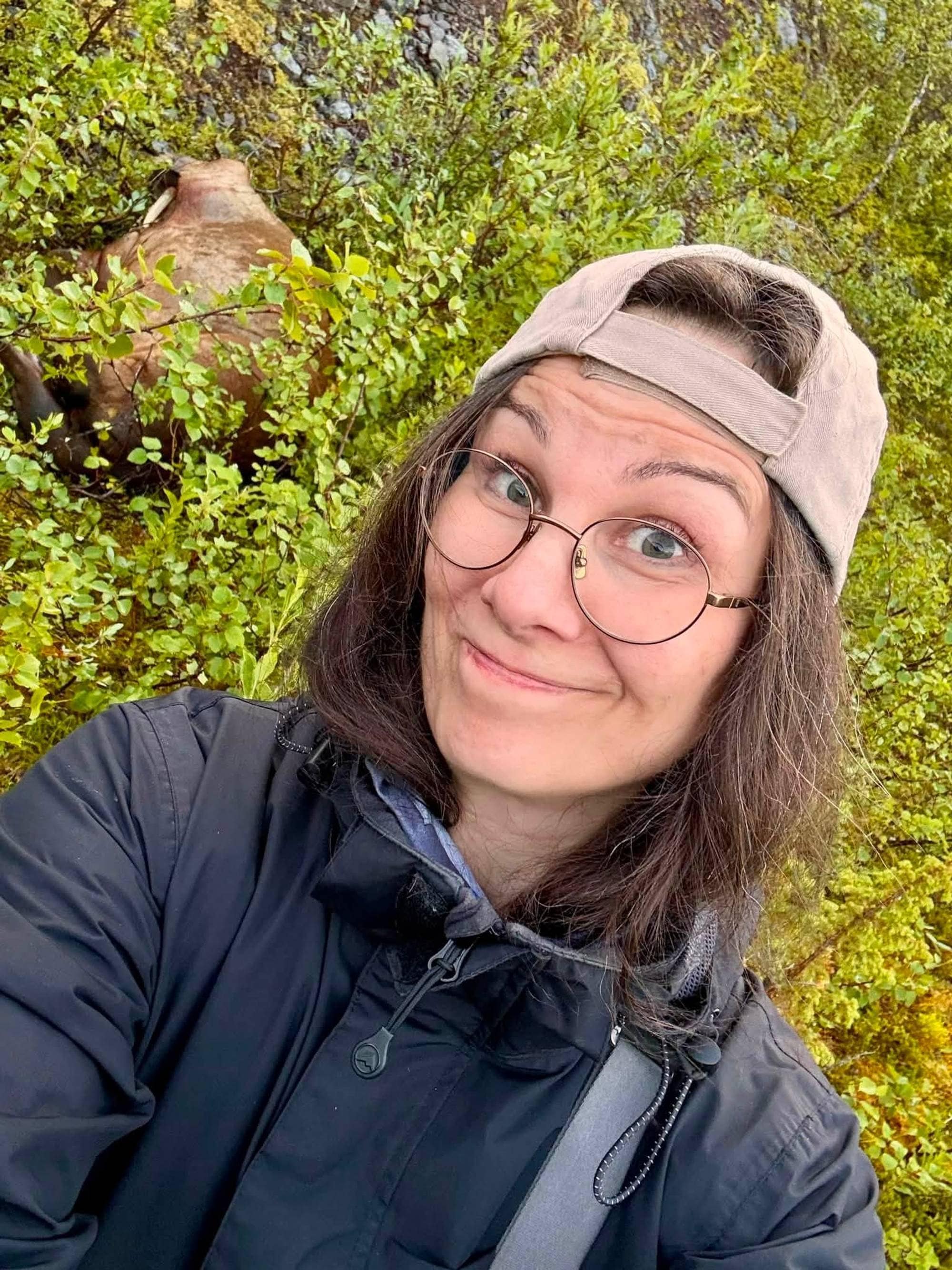 En dame med capsen bak frem tar en selfie med en hvalross som ligger i skogen.