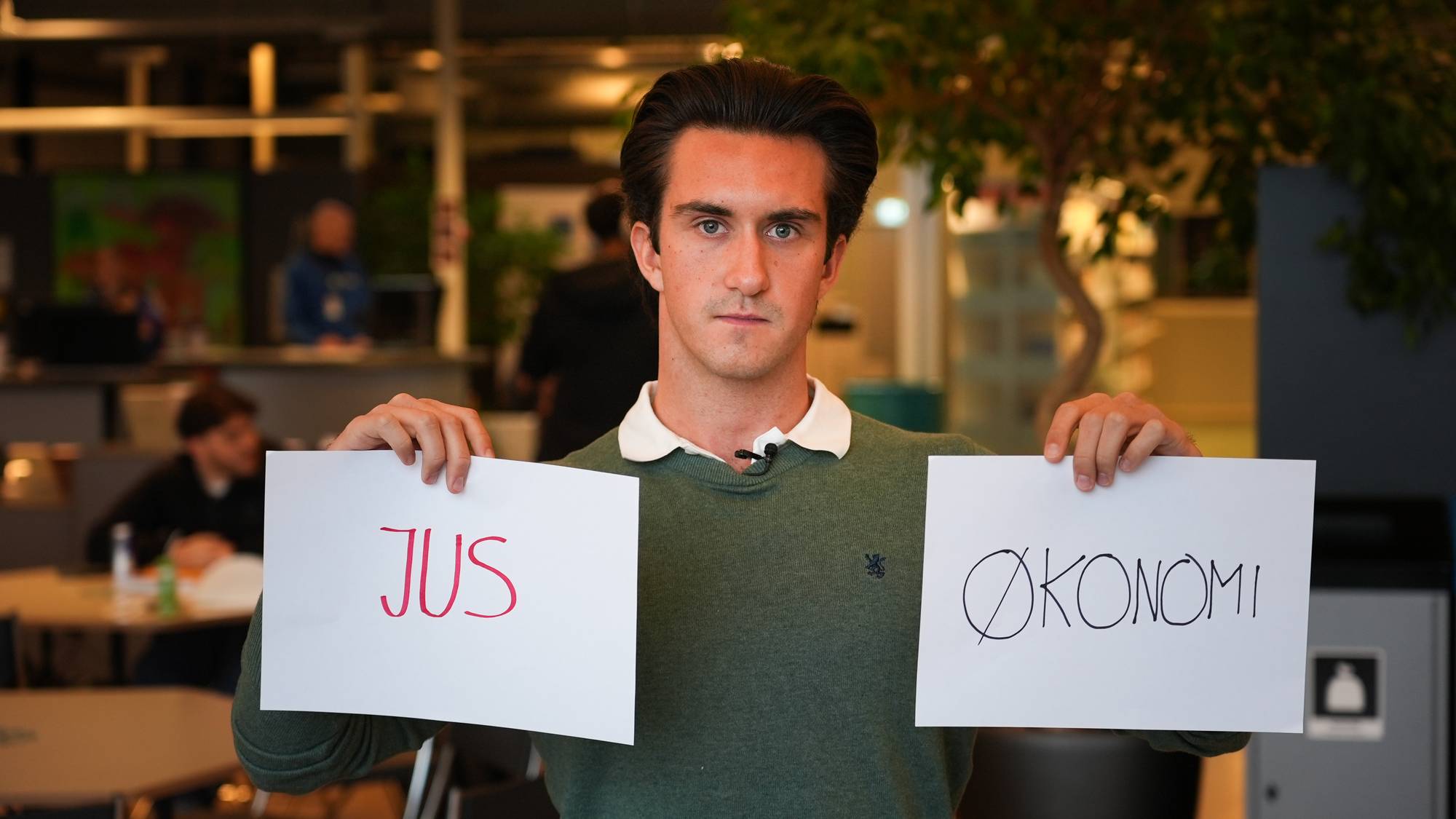 En ung mann som holder opp to ark. Det står "jus" på det ene arket og "økonomi" på det andre.