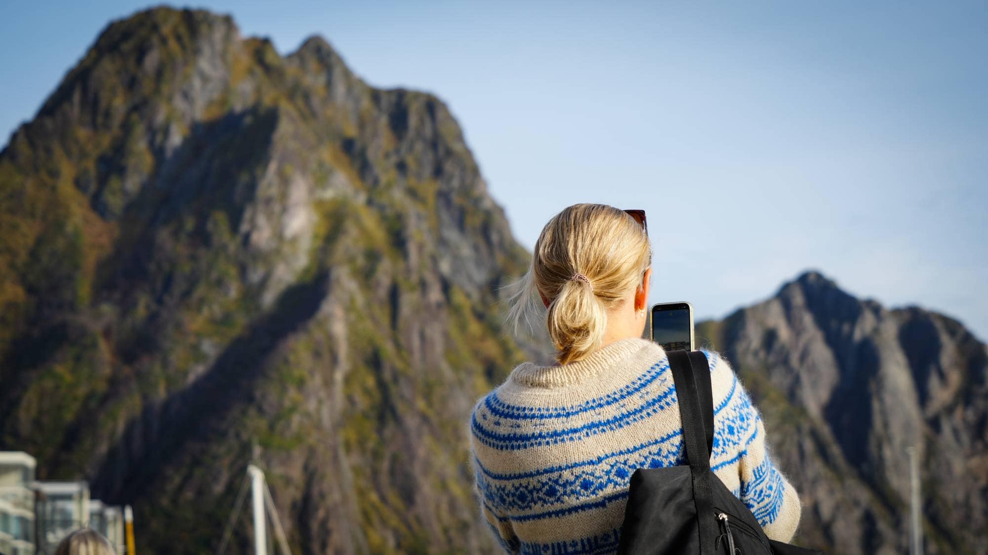 Turister på kaia i Svolvær som tar bilder av fjell og fjord i Lofoten. 