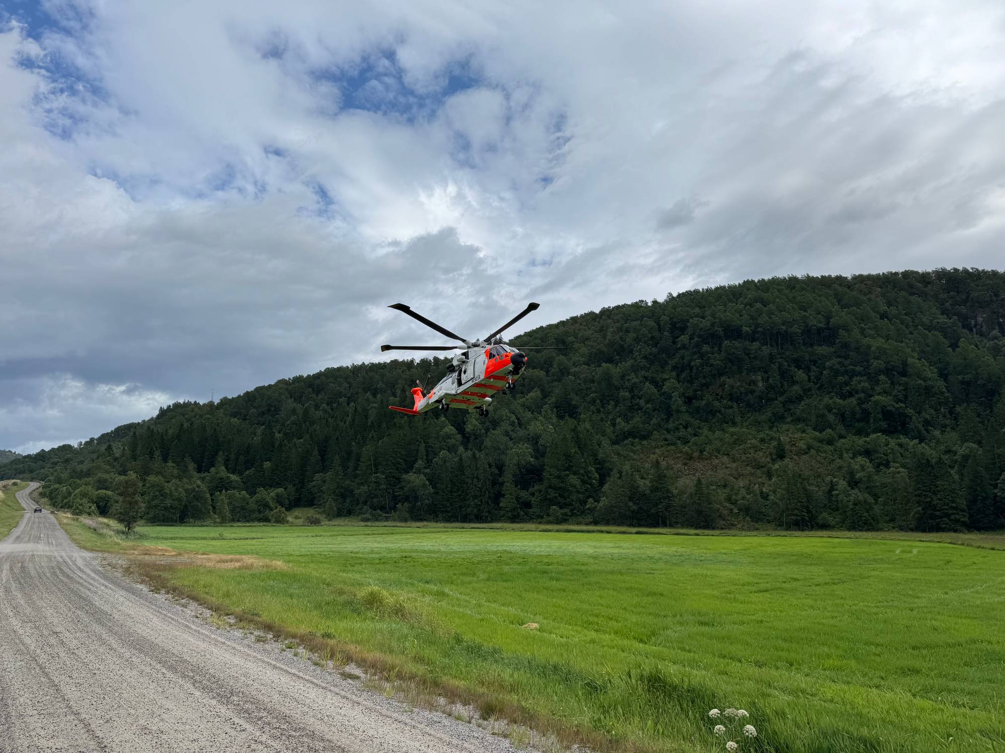 Et redningshelikopter lander på en gressplen ved siden av en grusvei.