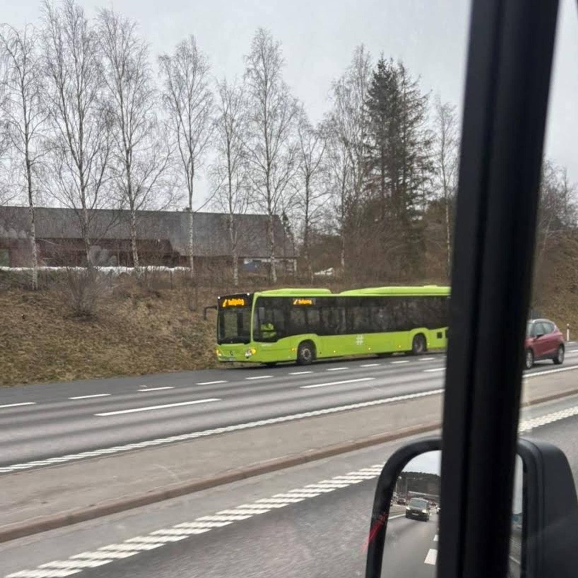 En grønn buss står i veikanten. Bildet er tilsynelatende tatt ut av et annet kjøretøy.