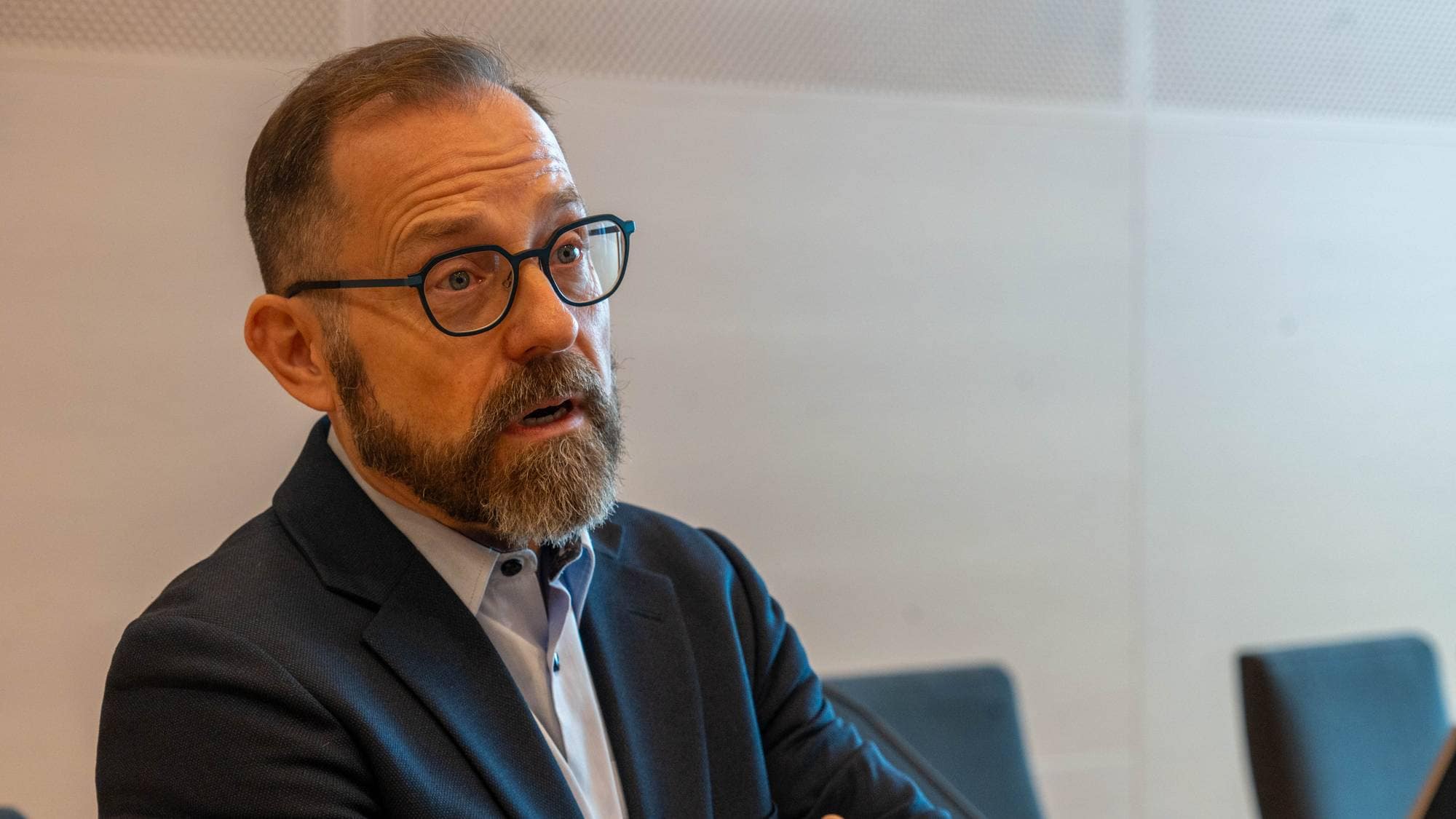 En mann med briller og skjegg sitter i en kontoromgivelse og snakker. 