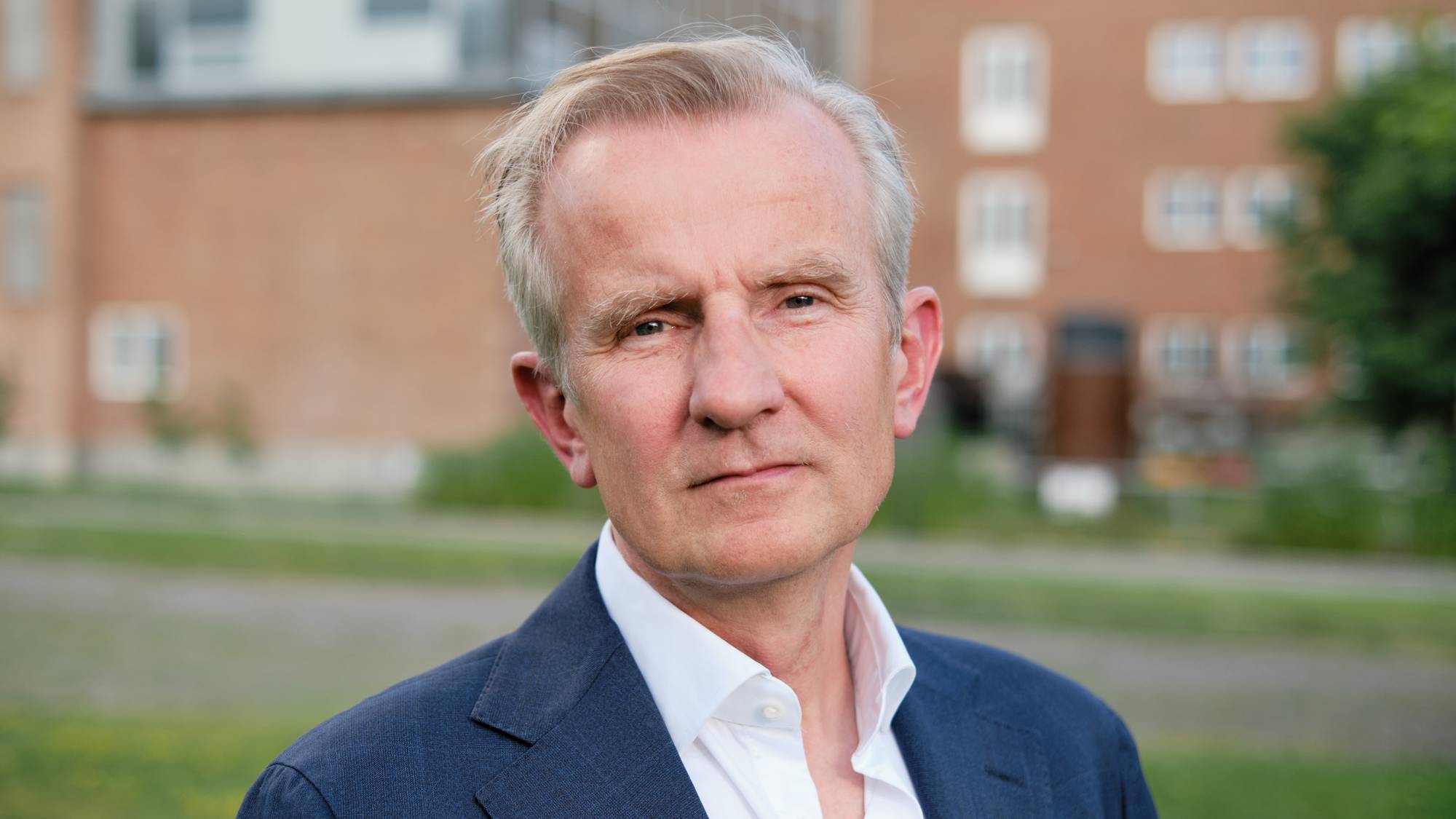 Portrett av mann i 50-årene med gråhåret sveis, iført hvit skjorte og mørk dressjakke utendørs. (Bildebeskrivelsen er laget av en KI-tjeneste)