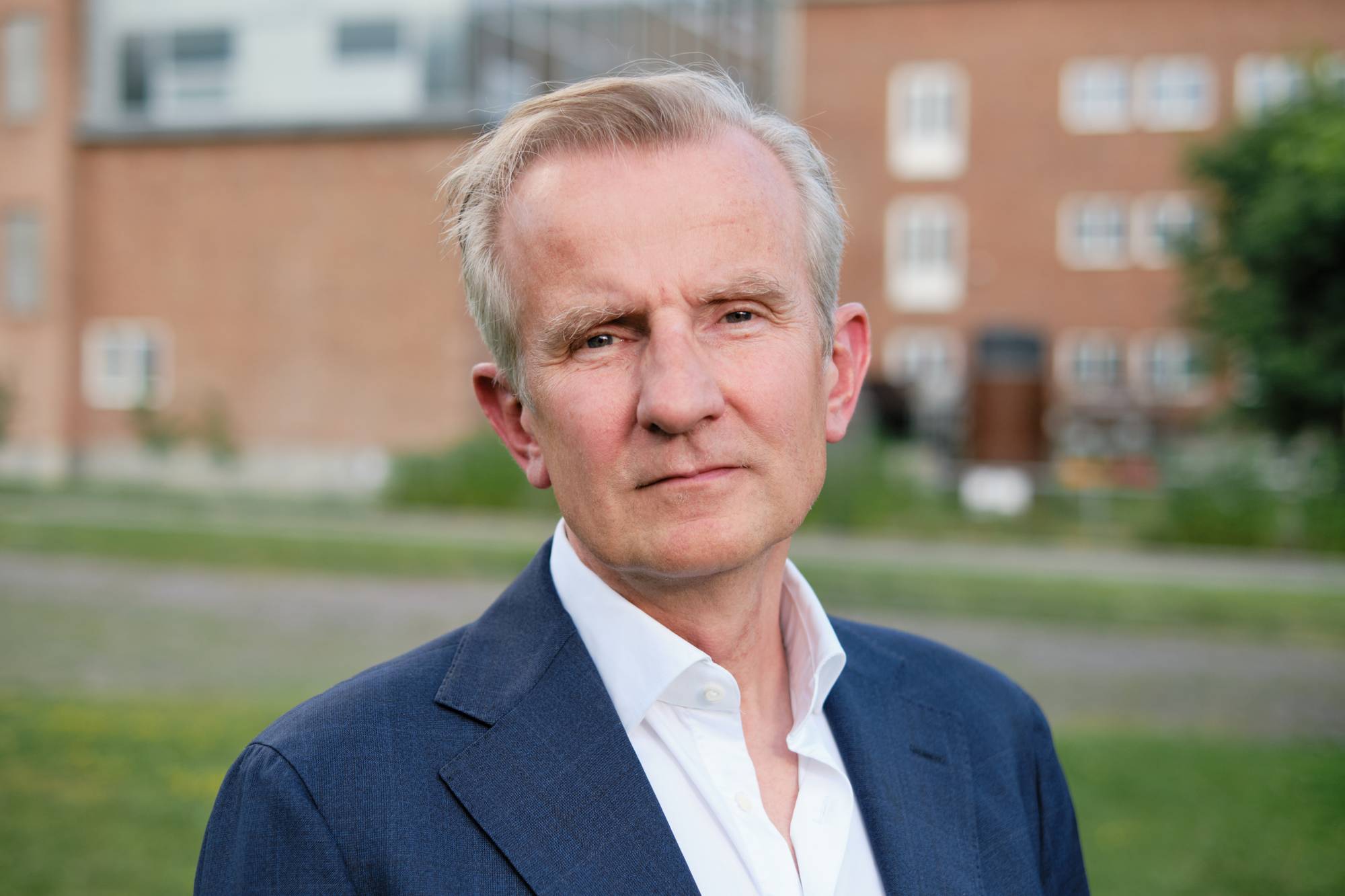Portrett av mann i 50-årene med gråhåret sveis, iført hvit skjorte og mørk dressjakke utendørs. (Bildebeskrivelsen er laget av en KI-tjeneste)