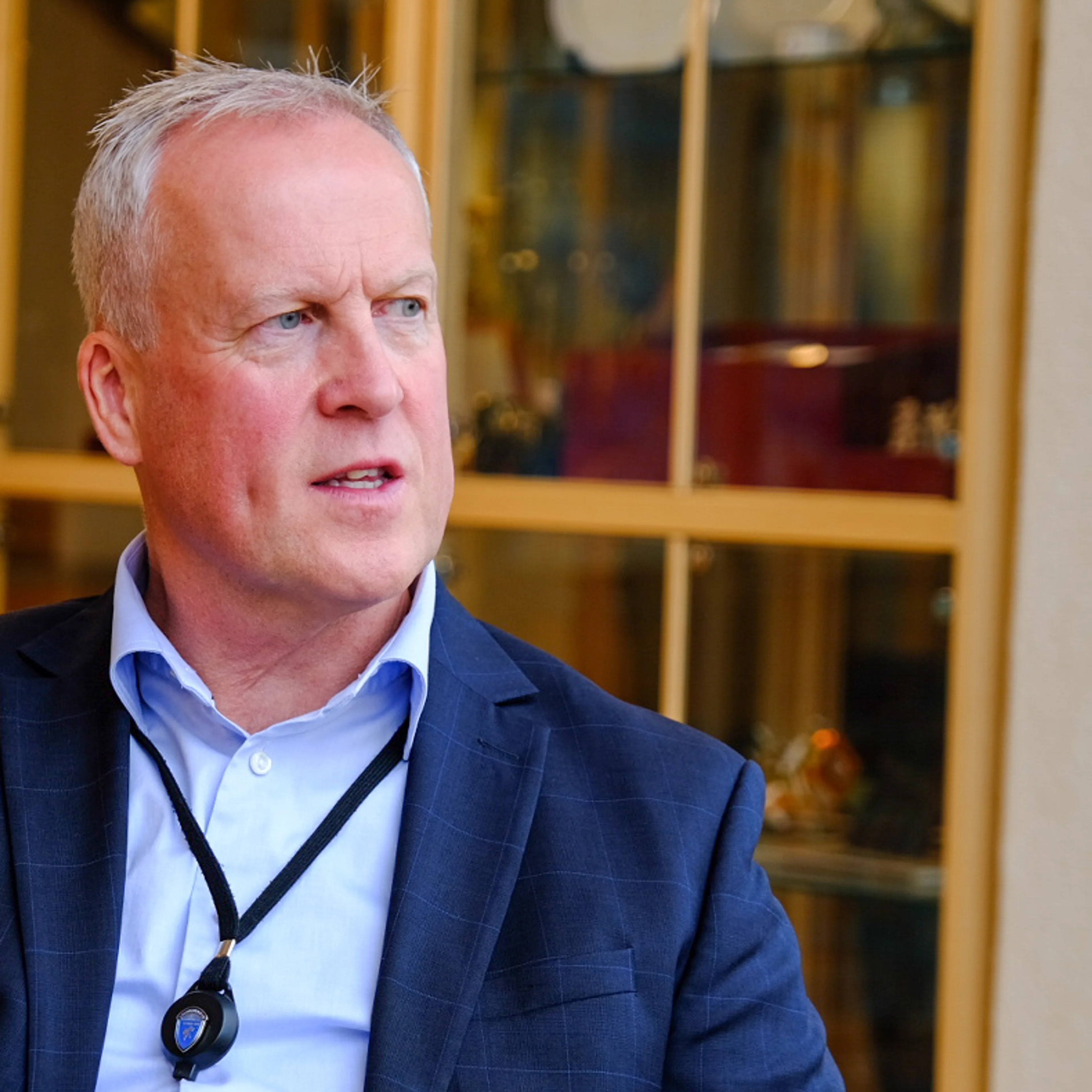 En mann i mørkeblå dress sitter i en lenestol i intervjusituasjon.