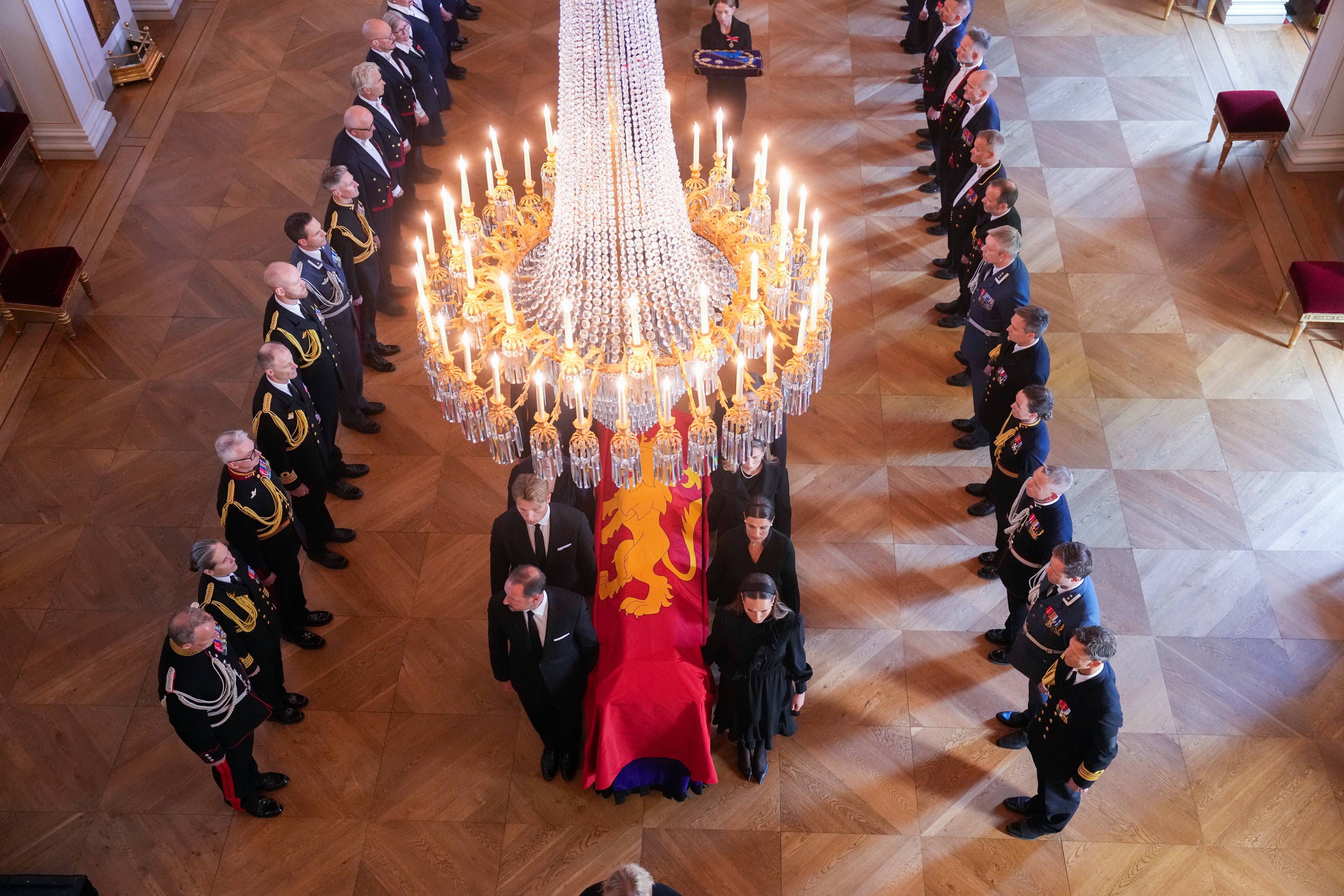 Kongelige og militære representanter samlet rundt en båre med riksvåpenet i Det kongelige slott. (Bildebeskrivelsen er laget av en KI-tjeneste)