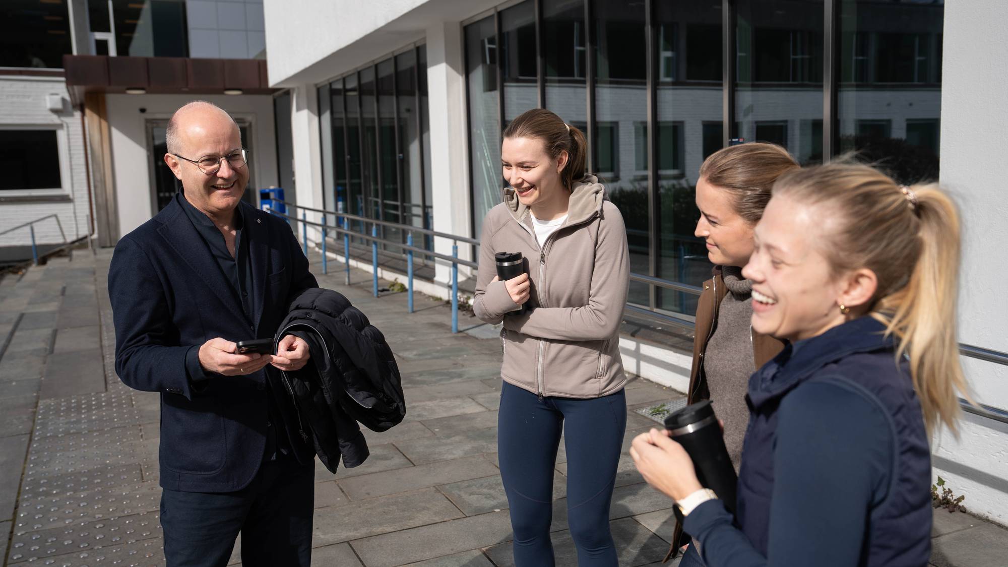 Taleekspert Trond Albert Skjelbred står til venstre i biletet. Han held ein telefon i handa, og smiler. Til høgre for han står tre kvinnelege studentar. Dei står vendt mot han, og ler. 