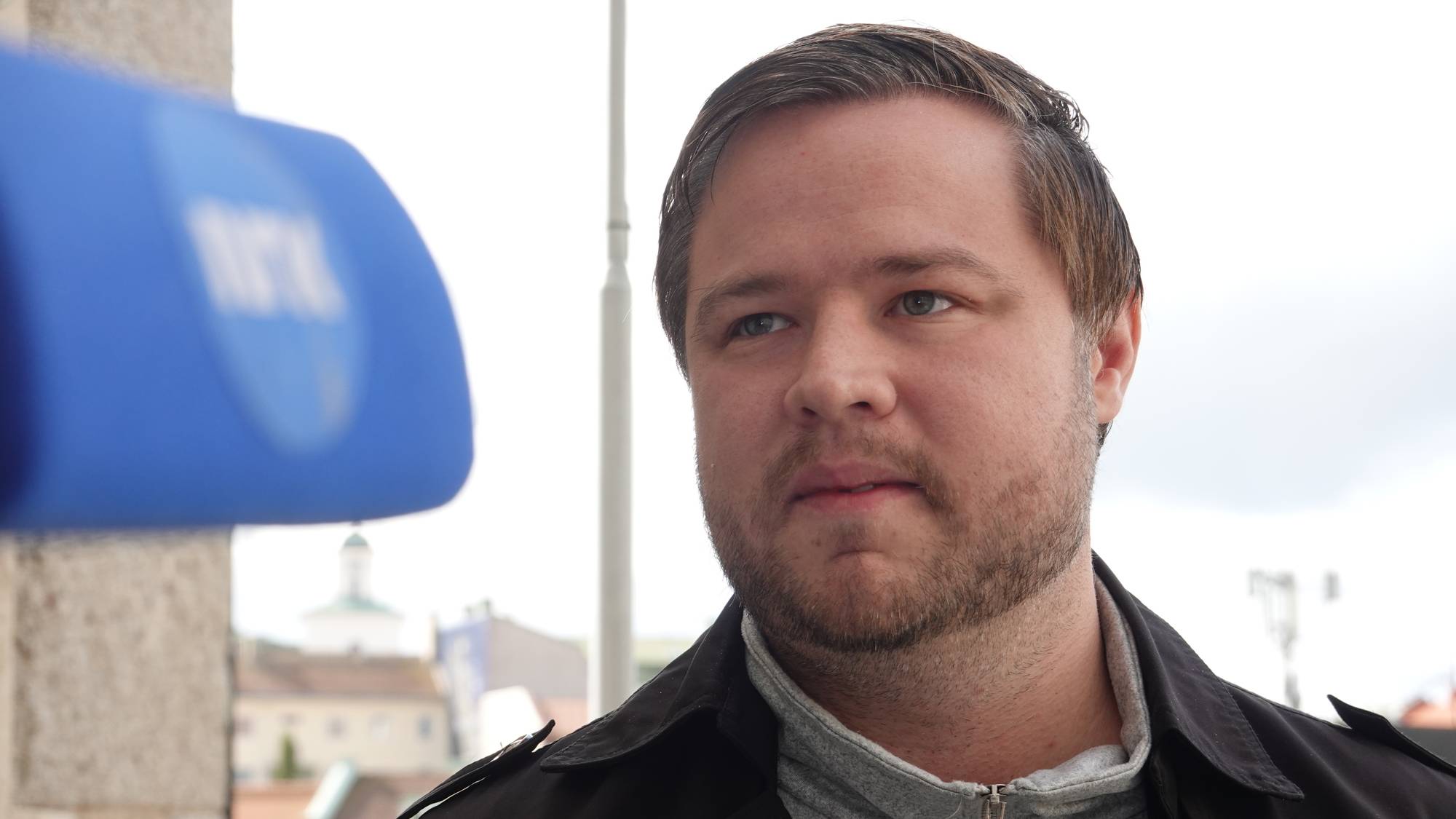 Mann intervjues med en NRK-mikrofon i forgrunnen. (Bildebeskrivelsen er laget av en KI-tjeneste)