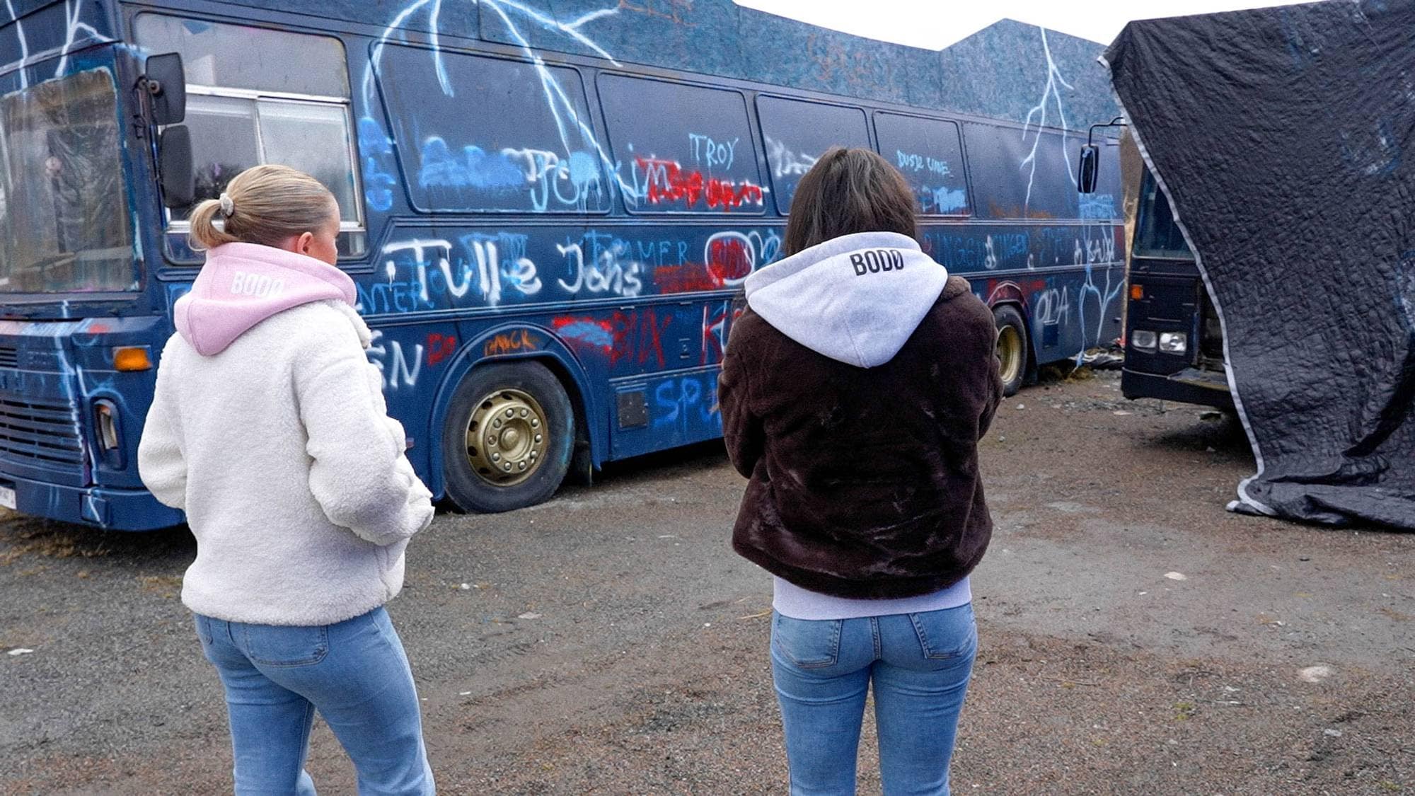 To jenter som står foran en russebuss med ryggen til