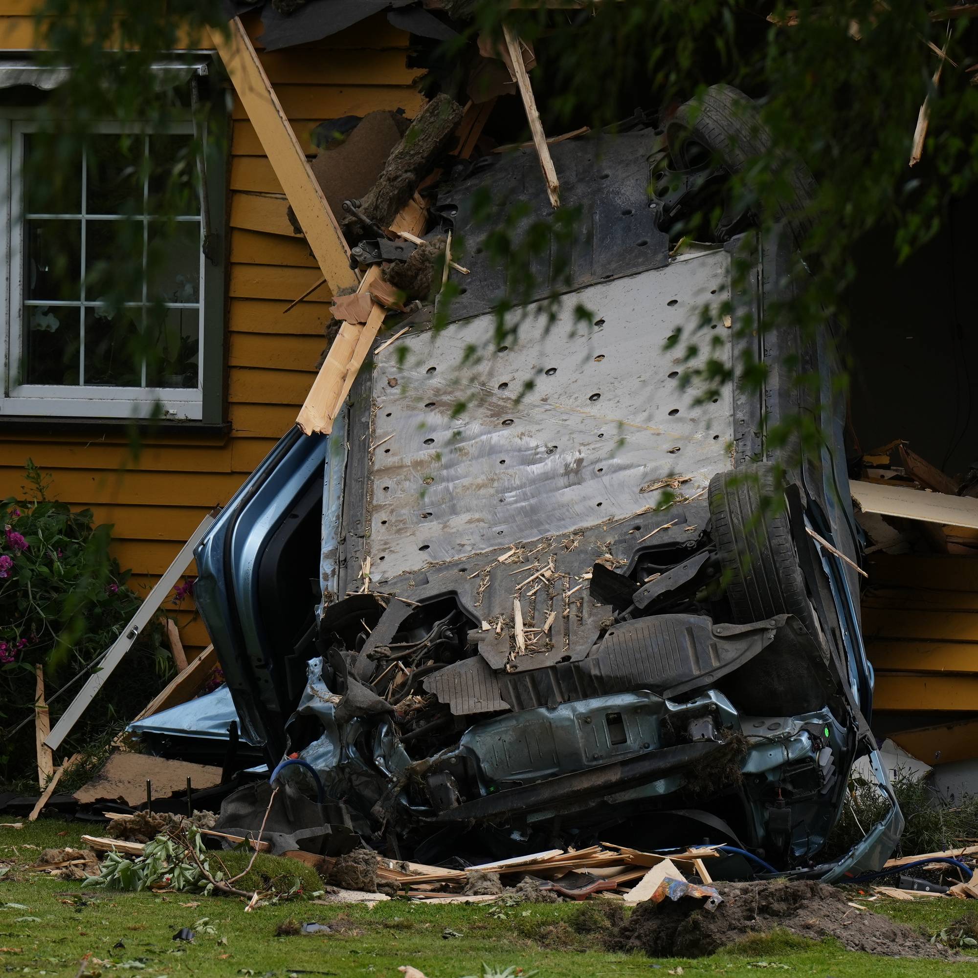 Bil krasjet inn i en gul enebolig. Bilen står på siden mot veggen med store materielle skader. (Bildebeskrivelsen er laget av en KI-tjeneste)