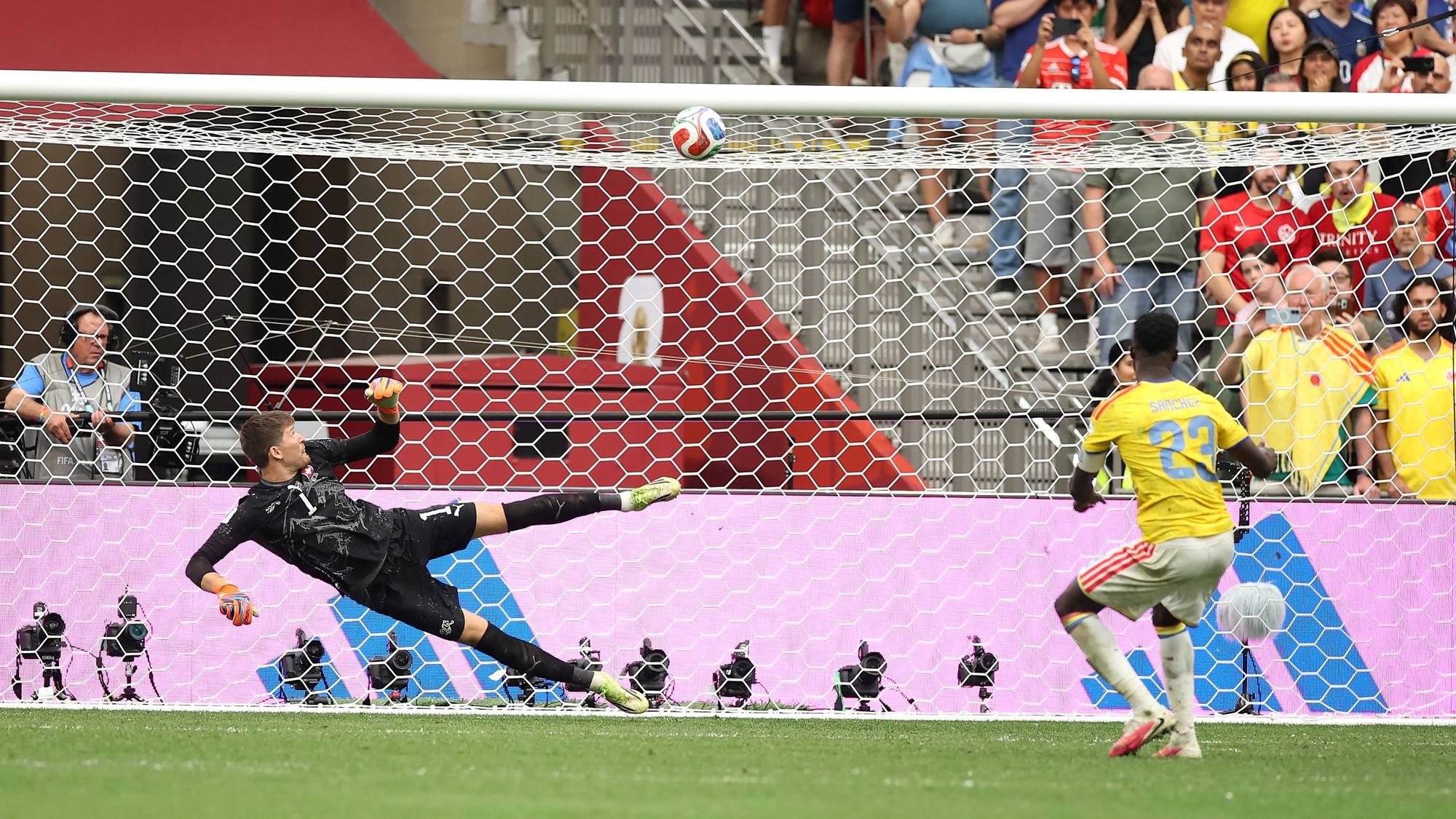 Keeperen kaster seg for å redde et skudd mens en colombiansk spiller ser på foran et fullsatt stadion. (Bildebeskrivelsen er laget av en KI-tjeneste)