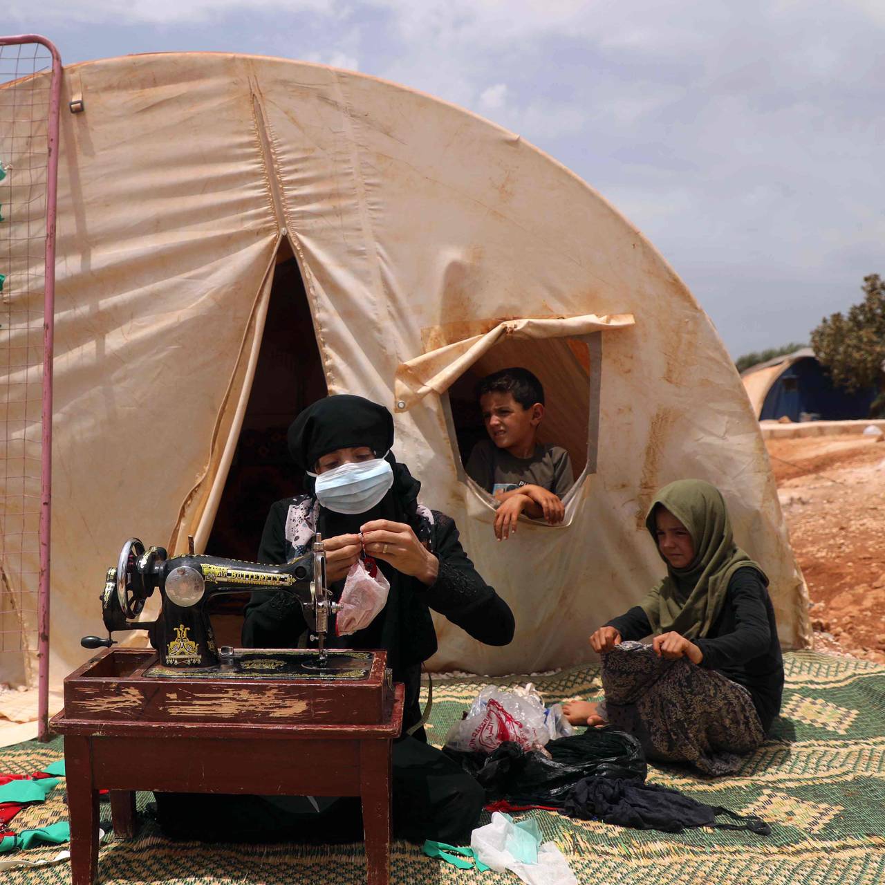 Den syriske kvinnen Umm Hussein syr munnbind i et telt i en flyktningleir i nordvest-Syria.