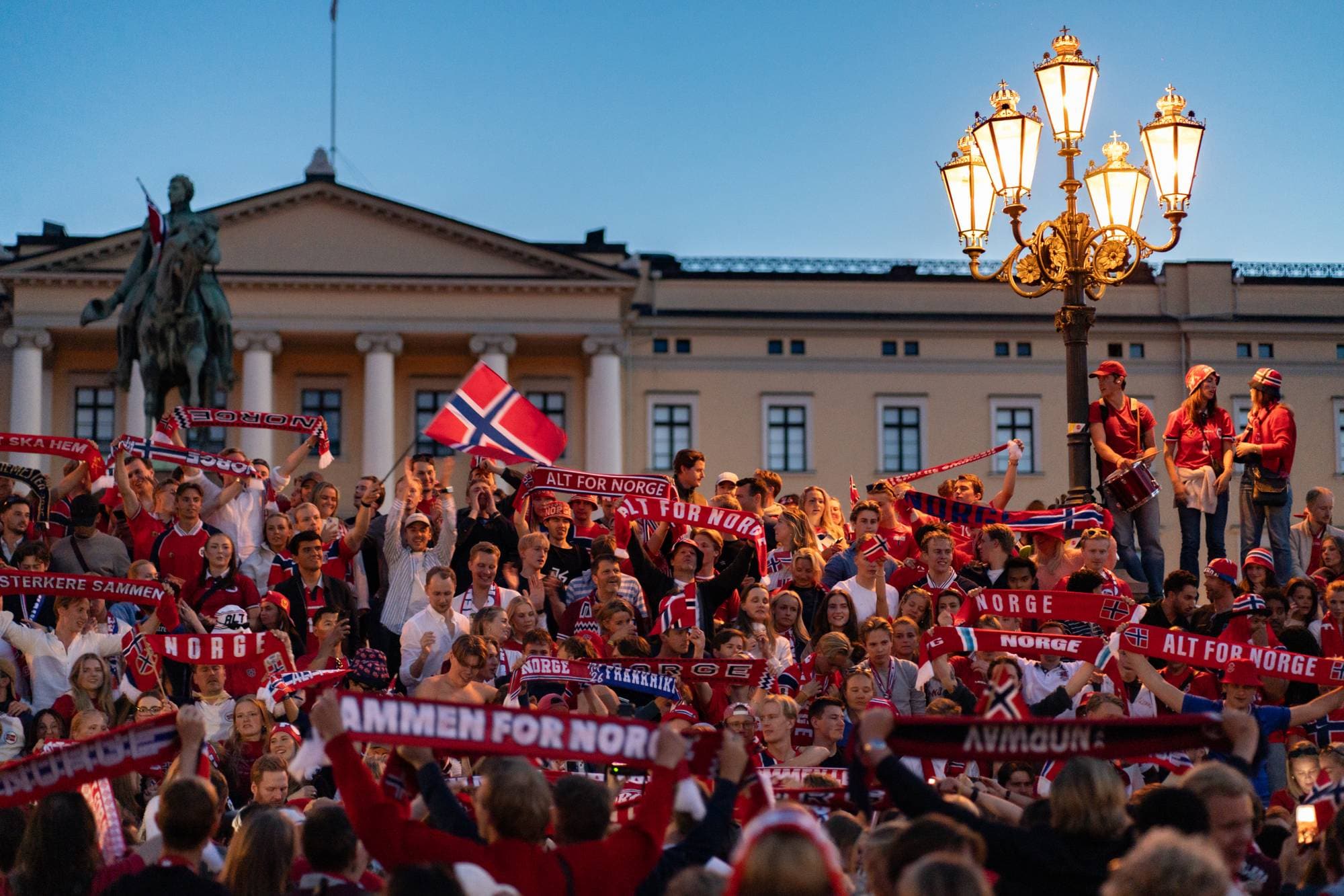 Folkemengde med norske flagg og skjerf foran Slottet i Oslo.