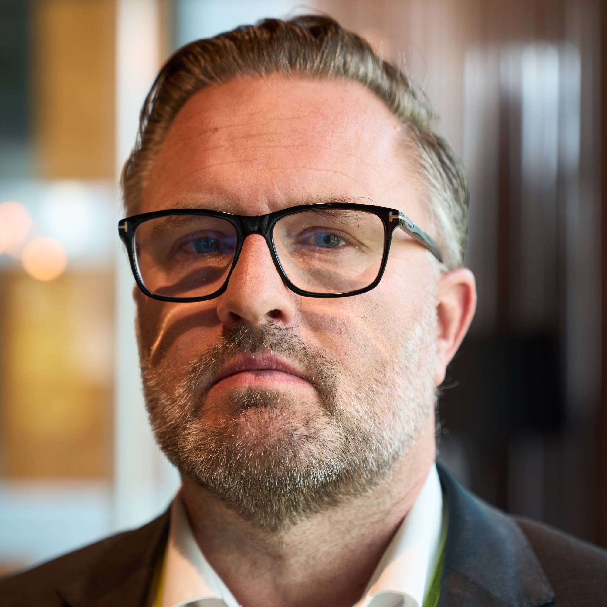 Portrett av en mann med skjegg og briller, ikledd dressjakke og skjorte. (Bildebeskrivelsen er laget av en KI-tjeneste)