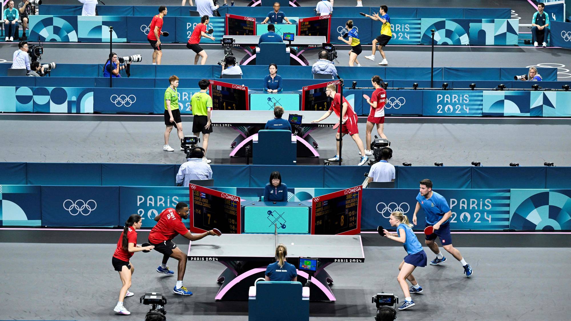 Bordtennisspillere i aksjon ved flere bord under OL i Paris 2024. (Bildebeskrivelsen er laget av en KI-tjeneste)