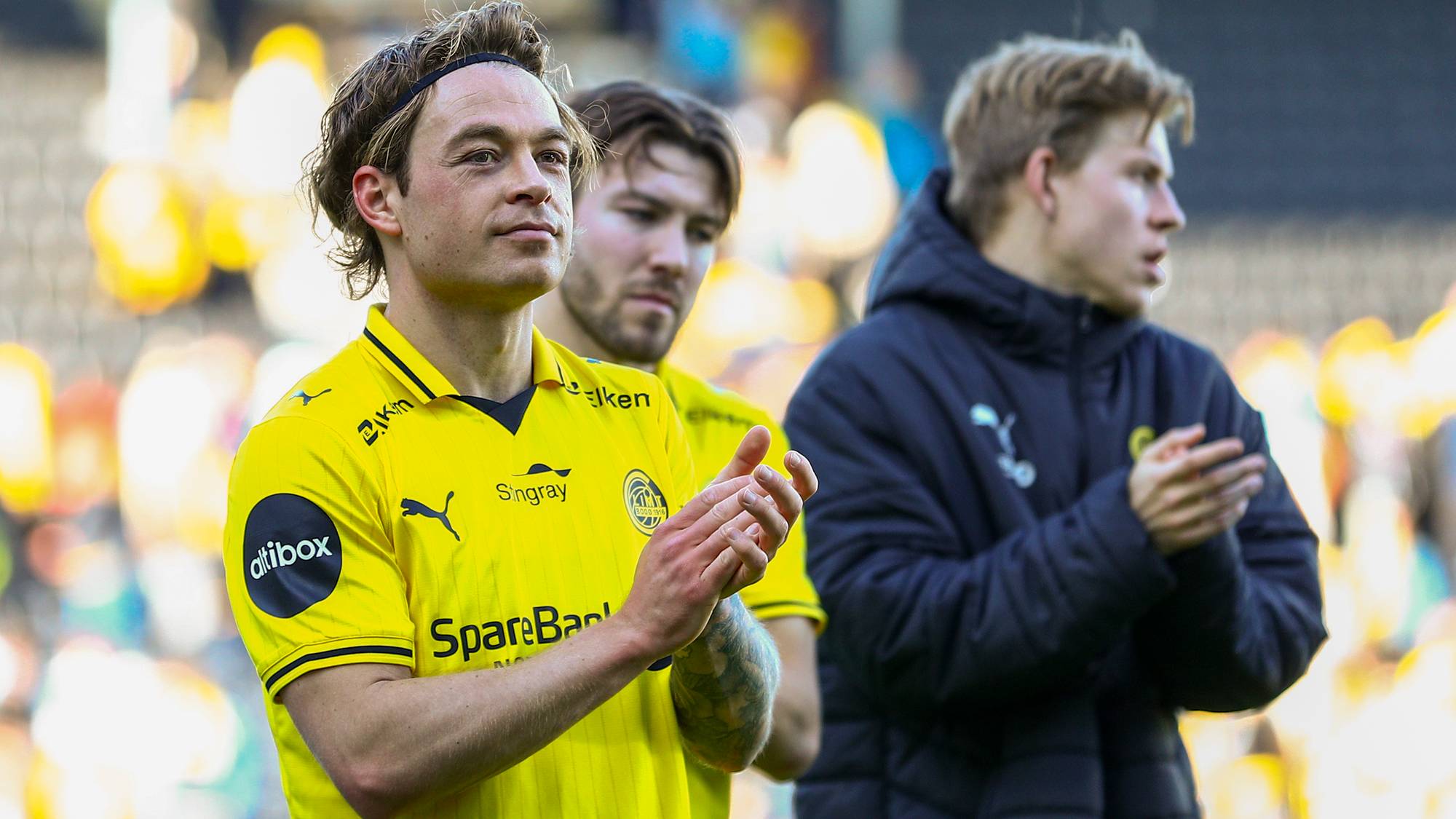 Tre fotballspillere kler gul drakt. To av dem klapper. Bildet er tatt utendørs under en kamp. (Bildebeskrivelsen er laget av en KI-tjeneste)