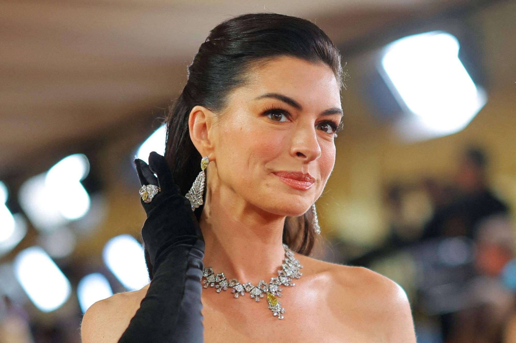 Anne Hathaway med mørkt hår og smykker, iført svarte hansker. (Bildebeskrivelsen er laget av en KI-tjeneste)