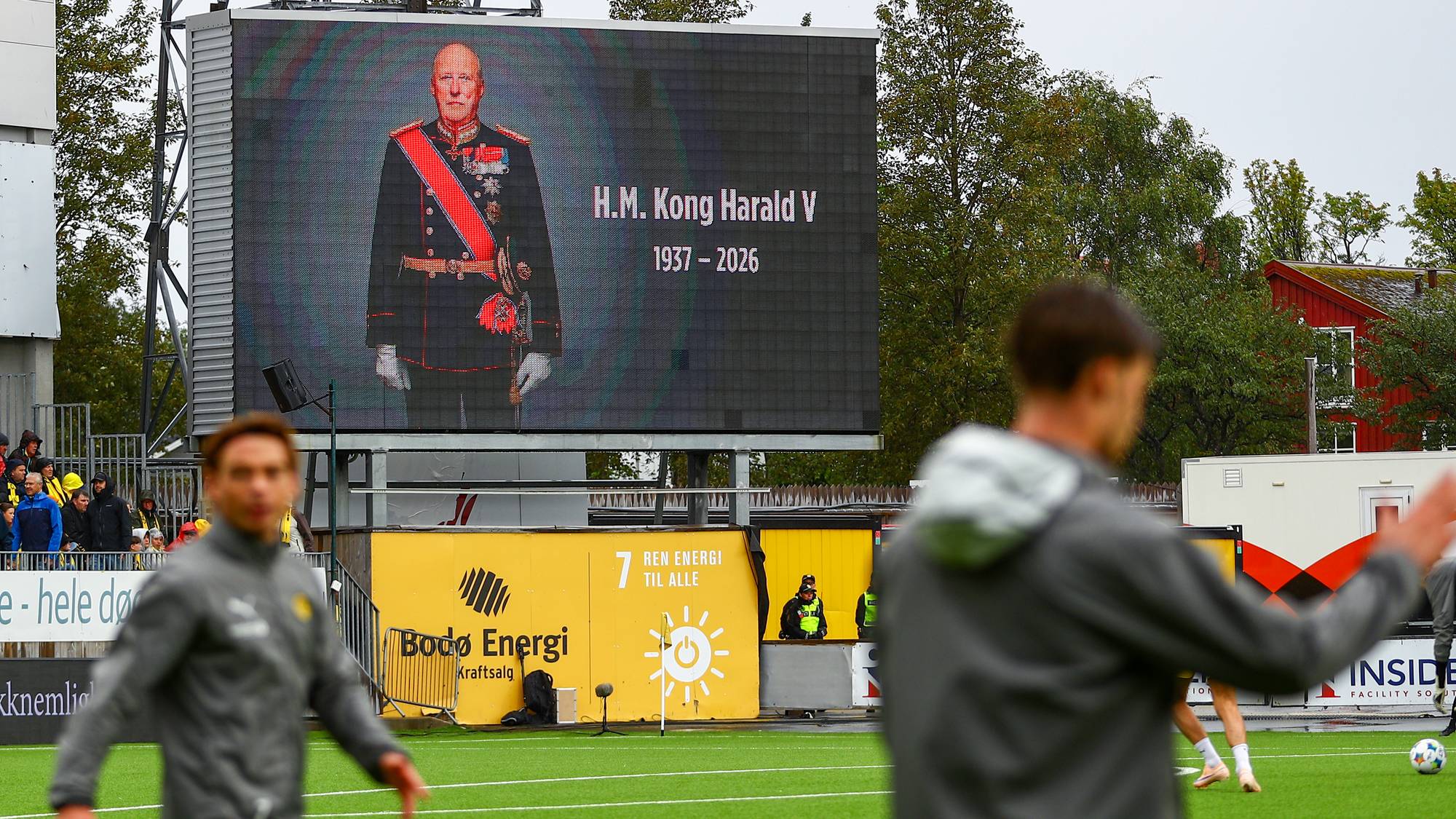 Storskjerm på fotballbane viser portrett av Kong Harald V med årstallene 1937–2026. (Bildebeskrivelsen er laget av en KI-tjeneste)
