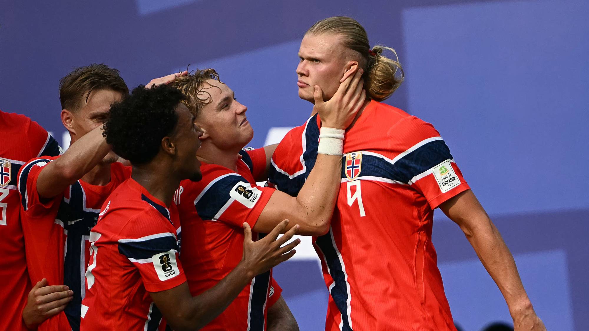 Fotballspillere på det norske landslaget feirer sammen i røde drakter med det norske flagget. (Bildebeskrivelsen er laget av en KI-tjeneste)