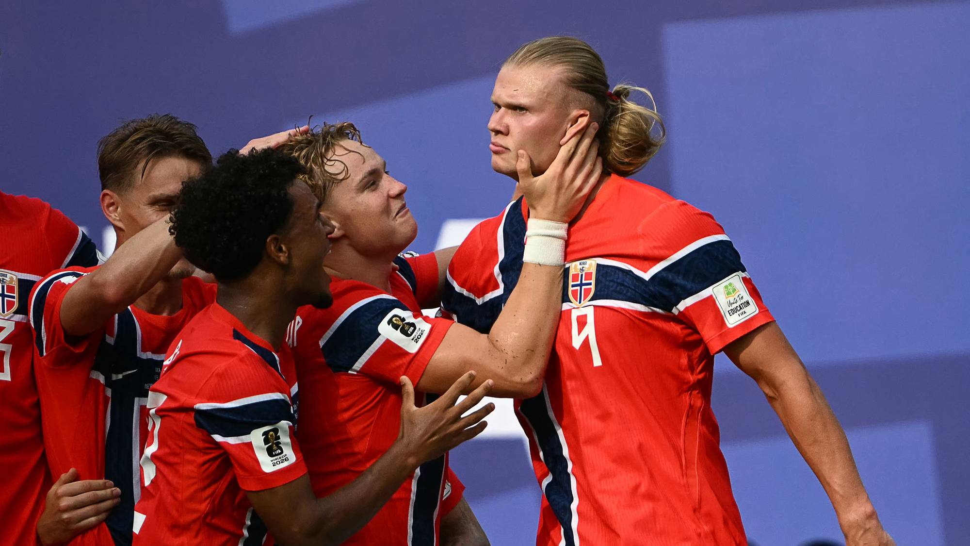 Fotballspillere på det norske landslaget feirer sammen i røde drakter med det norske flagget. (Bildebeskrivelsen er laget av en KI-tjeneste)