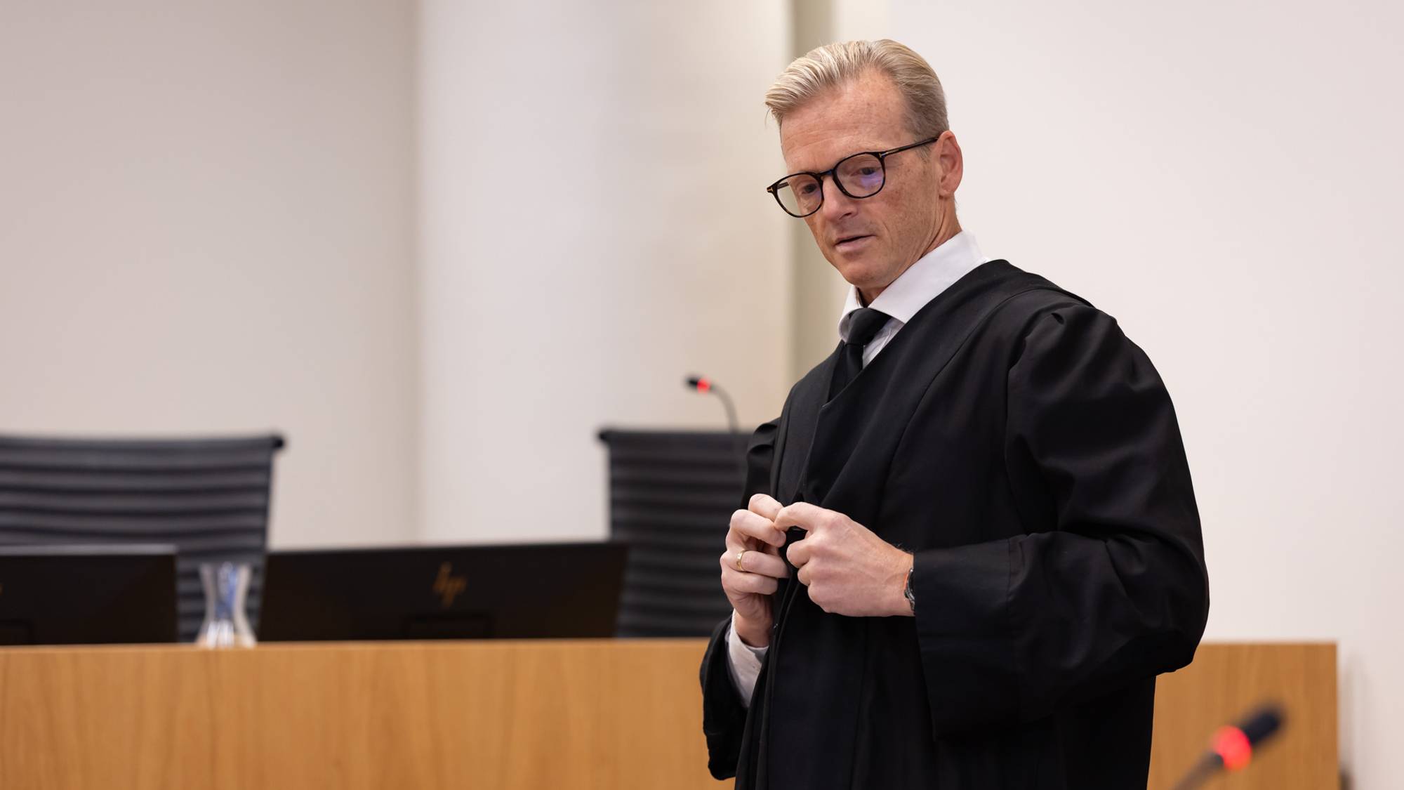 Forsvarer Fredrik Brodwall er iført svart kappe. Han har akkurat tatt den på seg og er i ferd med å ta igjen den siste knappen. Han kikker forsiktig nedover