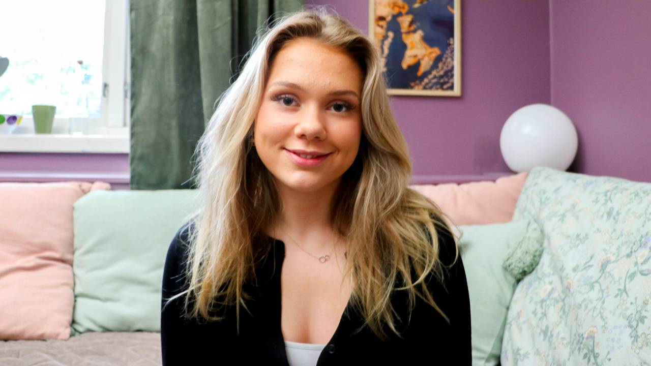 Ei jente sit i ei seng og ser mot kamera og smiler.