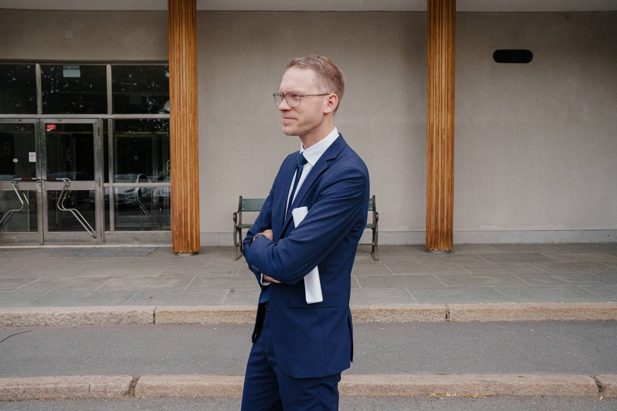 En mann i dresss holder en rull med papirer og ser mot siden