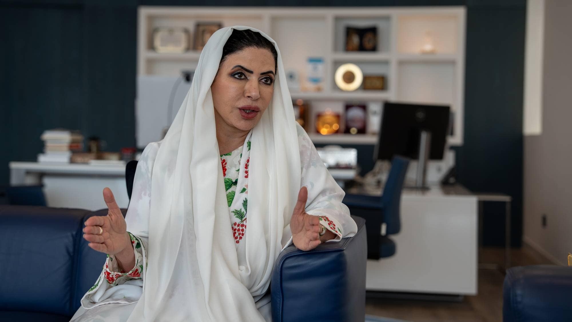 Kvinne med hvit hijab sitter i en blå sofa og snakker