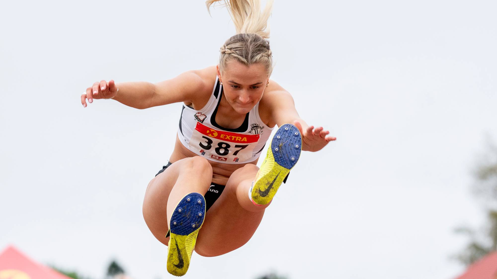 En kvinne i en hvit sportstopp hopper lengde i en friidrettskonkurranse. (Bildebeskrivelsen er laget av en KI-tjeneste)