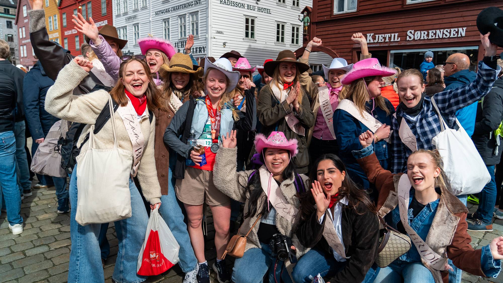 Maria Victoria Lothe (i kvit cowboyhatt) saman med utdrikkingslaget sitt foran Bryggen, etter å ha deltatt i Bergen City Marathon 2026.