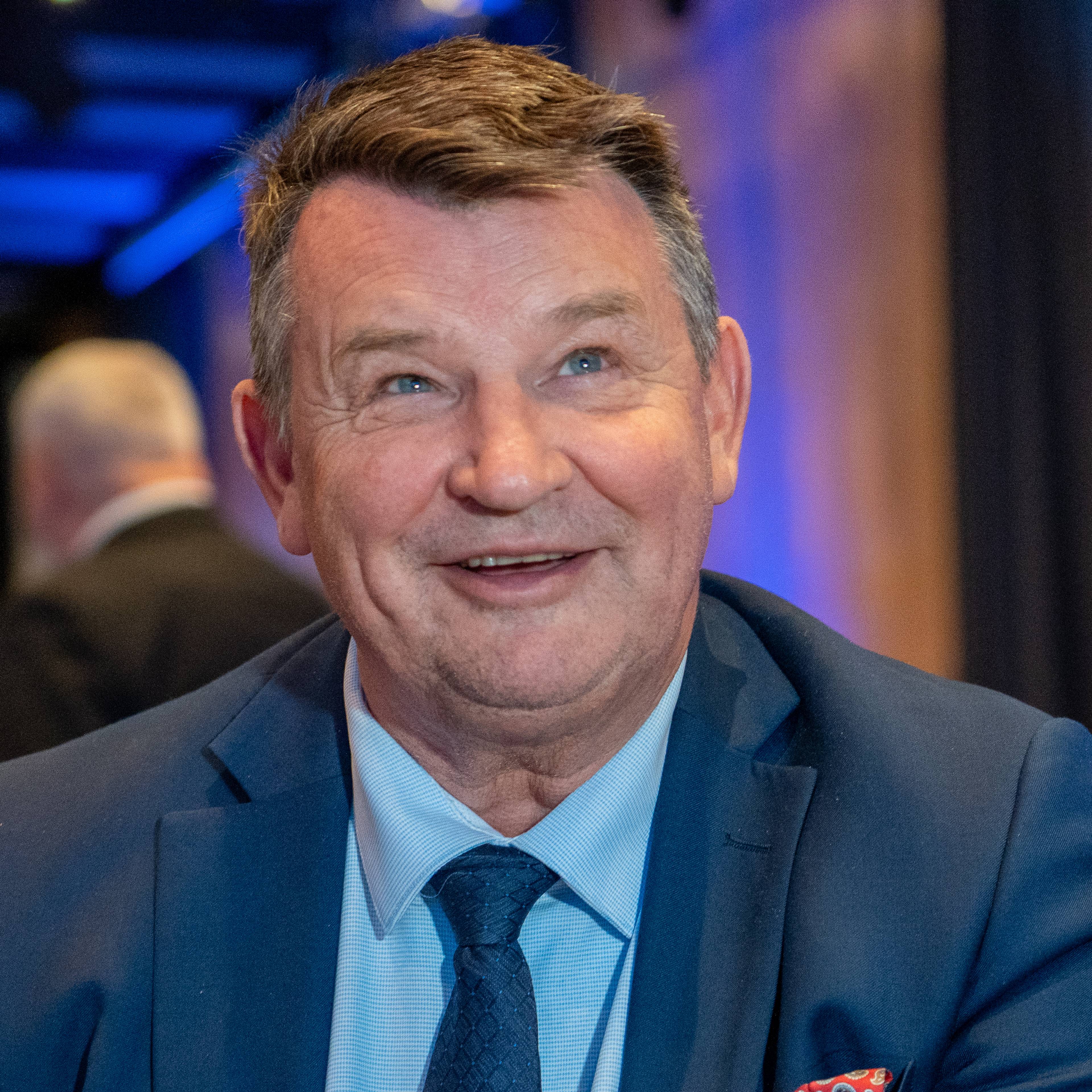 Nærbilde av mann som smiler og ser skrått oppover i en festsal