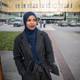 William Jobling / NRK En kvinne i mørk frakk og hijab står på fortauet utenfor en bygning. I bakgrunnen er det biler parkert og folk som krysser gaten. Området ser urbant ut med gressplener og halvmørkt vær. Bygningens fasade er i gule og glassfargede materialer.