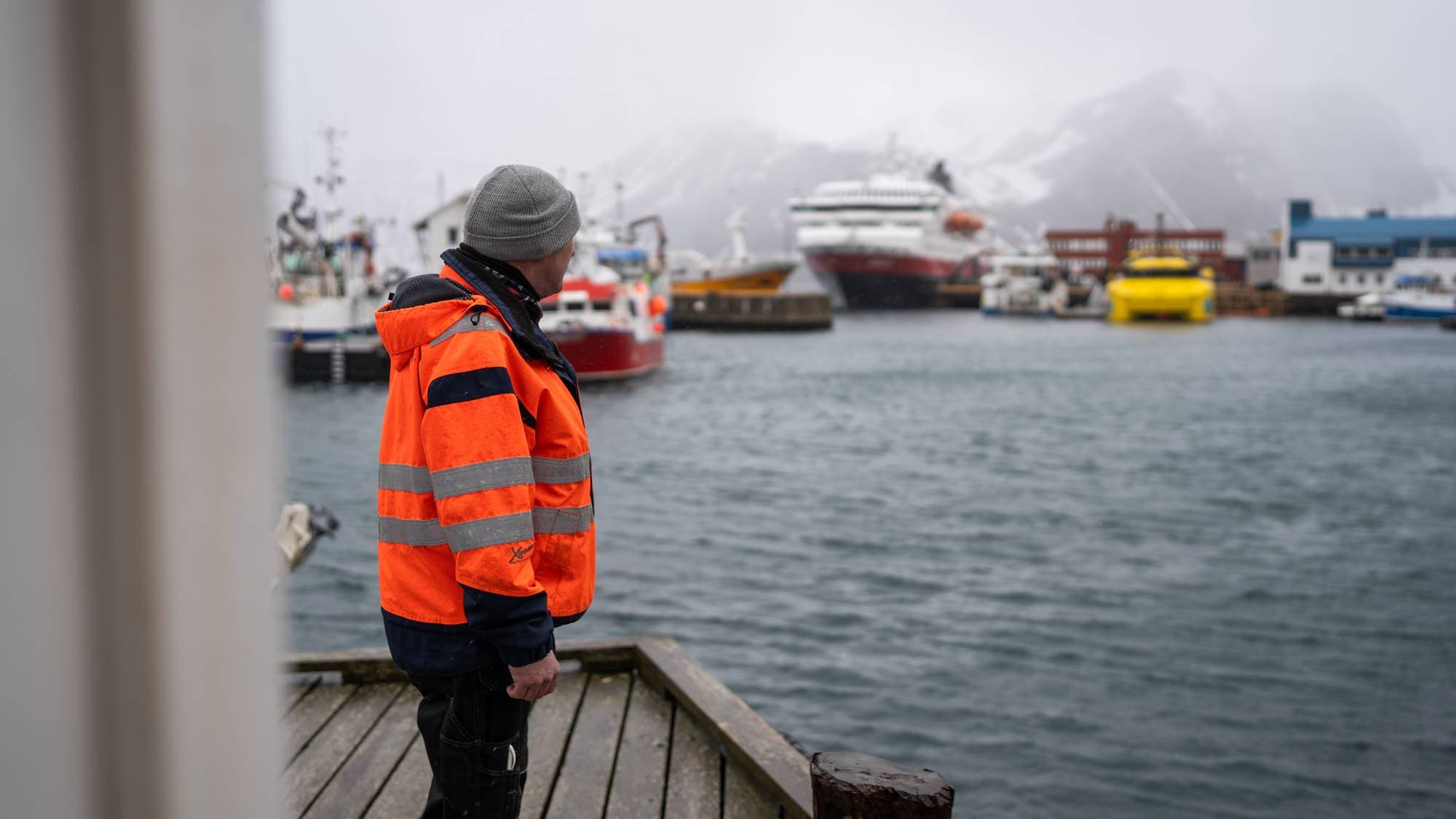 Arve Olsen står på kaia og ser på hurtigruta MS Nordlys i Honningsvåg. Gårtt, lavt skydekke og snø i fjella