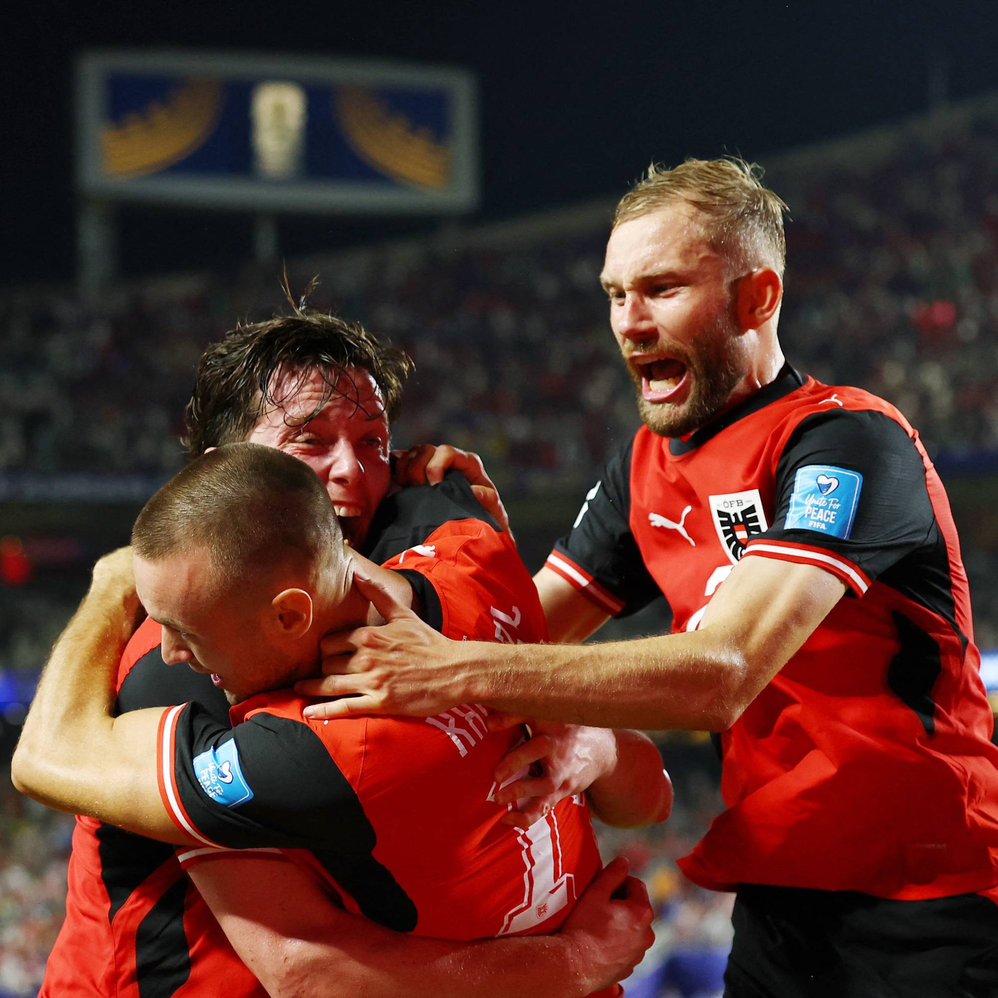 Østerrikske fotballspillere i røde drakter feirer mål ved å klemme hverandre på banen. (Bildebeskrivelsen er laget av en KI-tjeneste)