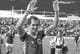 Scanpix En fotballspiller vinker til publikum. Han er iført en rød trøye med et norsk flagg på brystet. I bakgrunnen står tilskuere på tribunen. En annen person med kamera går forbi. (Bildebeskrivelsen er laget av en KI-tjeneste)