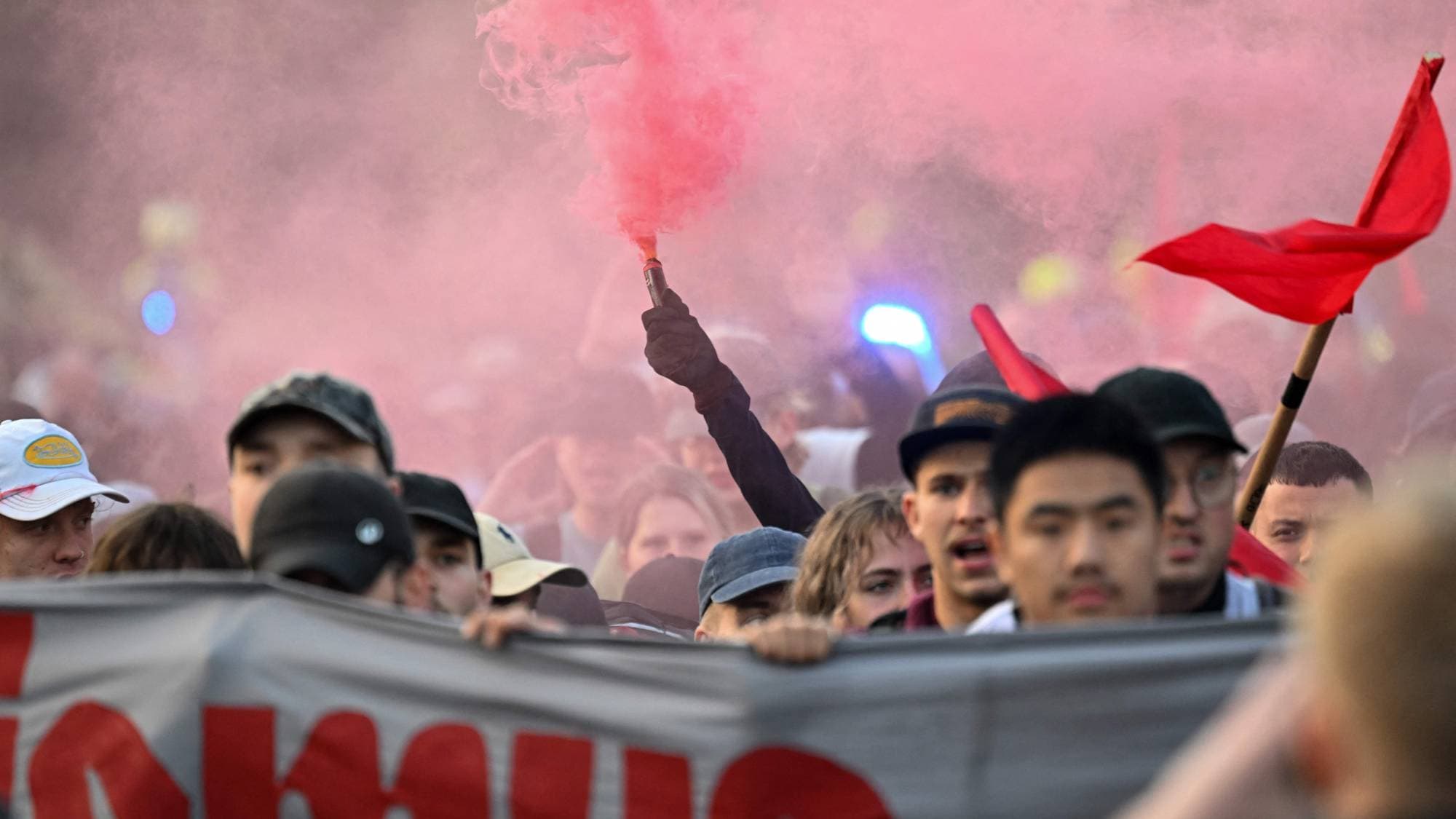 Personer i demonstrasjonstog holder et banner og brenner rødt bluss. (Bildebeskrivelsen er laget av en KI-tjeneste)