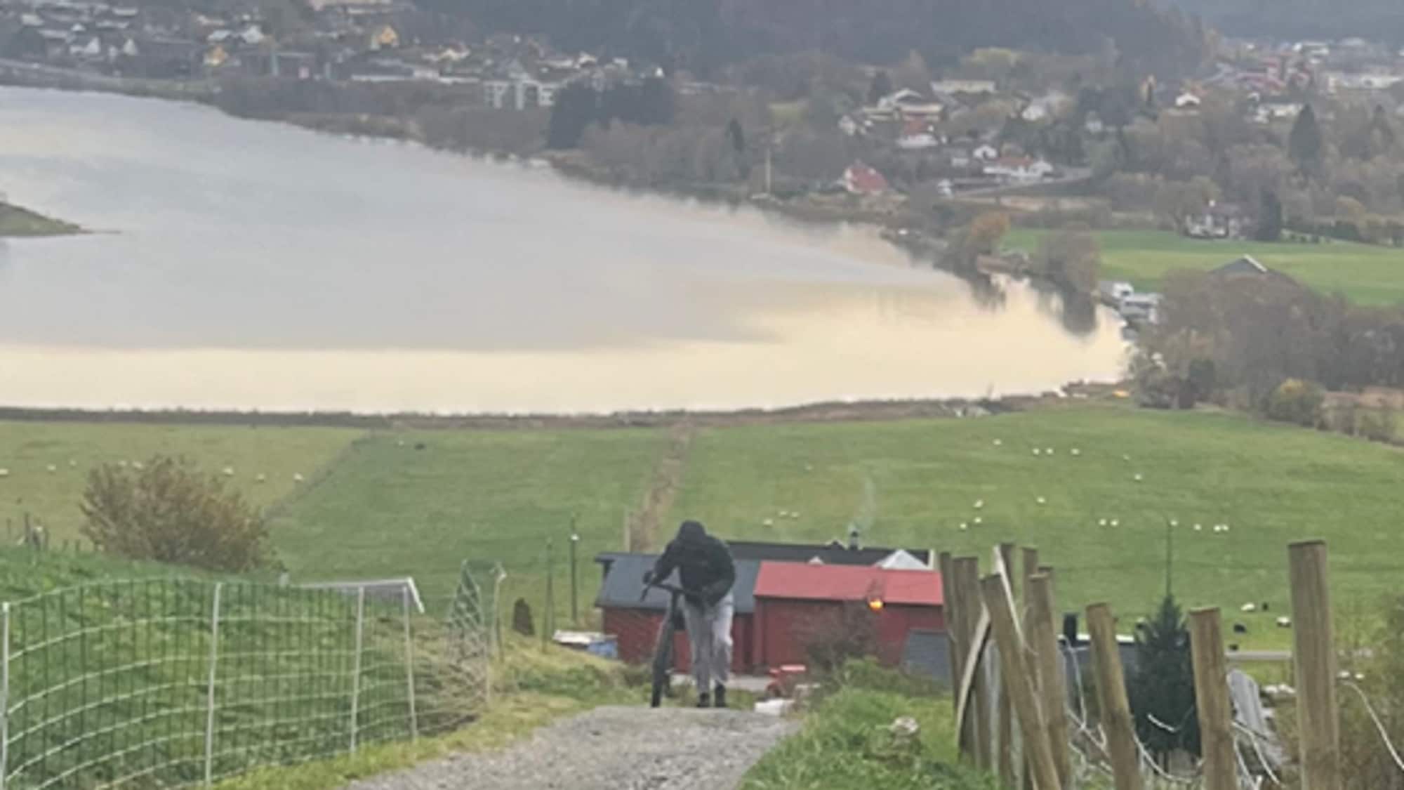 person triller sykkel opp en grusvei med marker rundt
