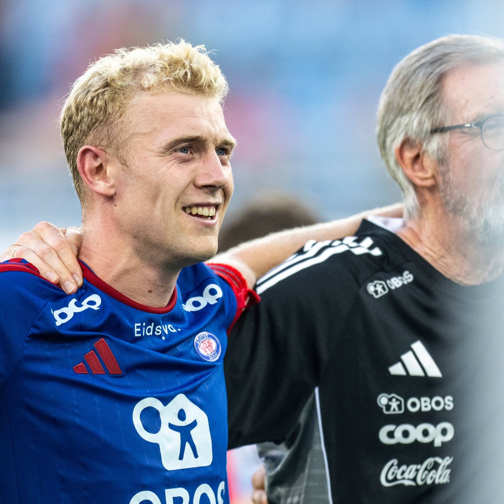 Fotballspiller og trener står skulder til skulder med armene rundt hverandre på en fotballbane. (Bildebeskrivelsen er laget av en KI-tjeneste)