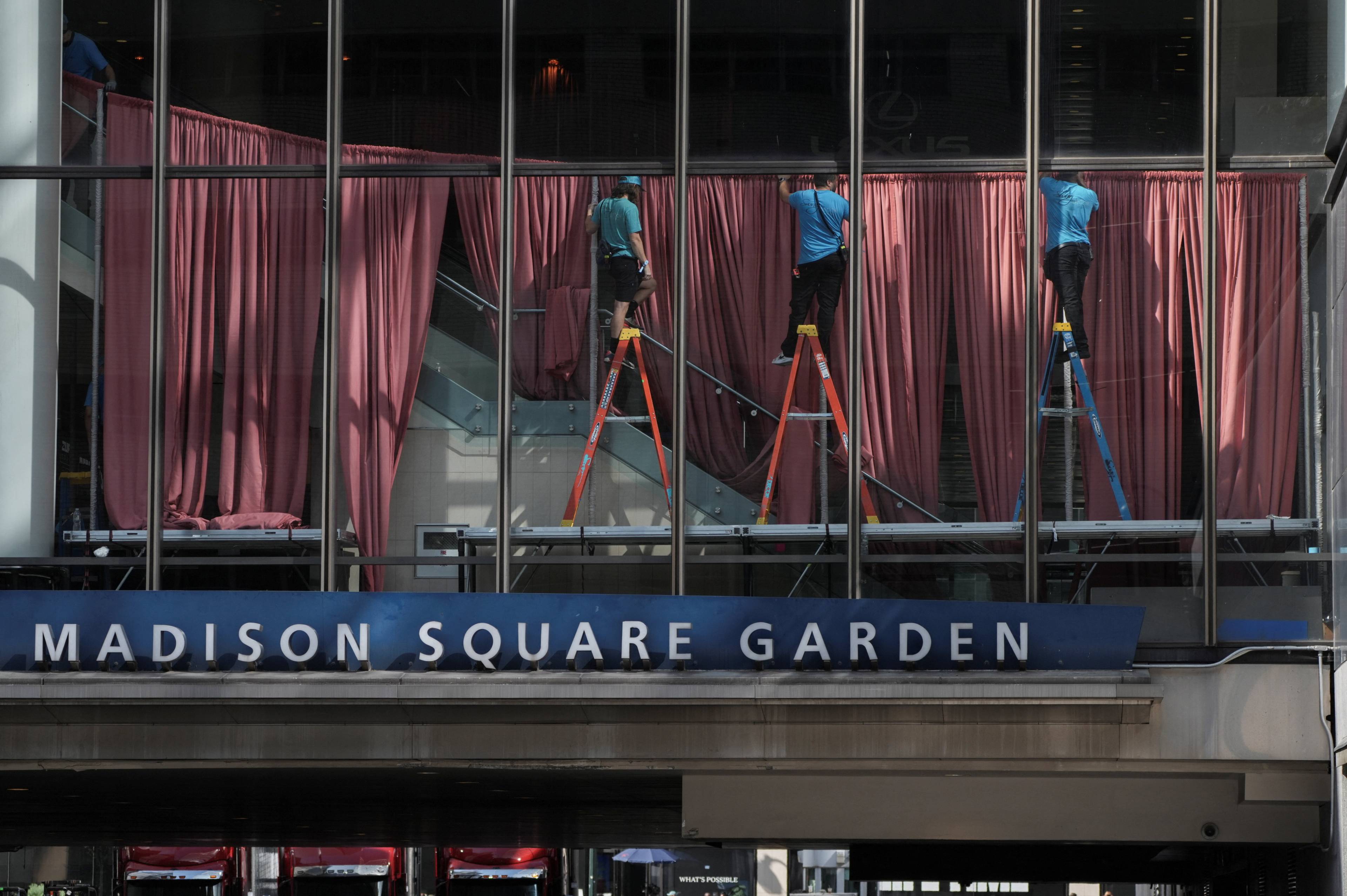 Arbeidere på stiger monterer røde gardiner i vinduene ved Madison Square Garden. (Bildebeskrivelsen er laget av en KI-tjeneste)