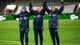Carina Johansen / NTB Tre personer i treningstøy står på en fotballbane og hever hendene i triumf. De smiler og viser glede. Bakgrunnen viser en stadion med tomme seter. Det er belysning og kunstgress på banen.